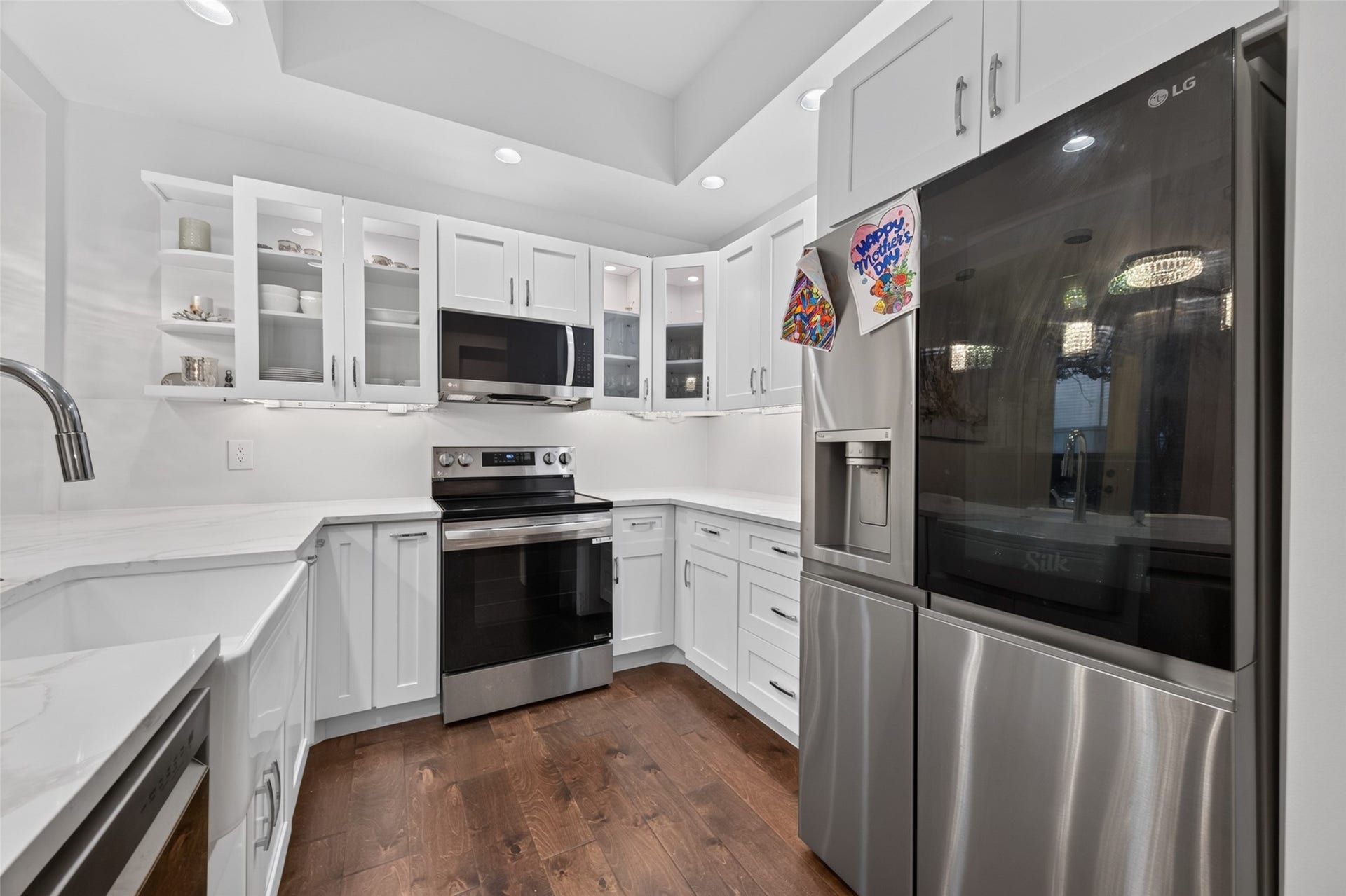 This kitchen features a modern design with white cabinetry, stainless steel appliances, and dark wood flooring. It includes a sleek refrigerator, built-in microwave, and ample counter space, offering a bright and functional cooking area.