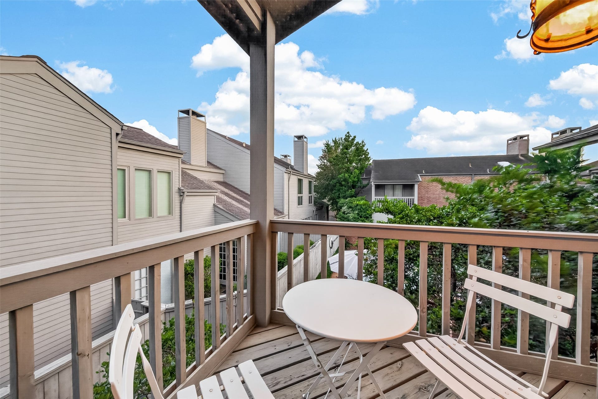 Charming balcony with a cozy seating area, offering views of neighboring homes and lush greenery. Perfect for relaxing outdoors.