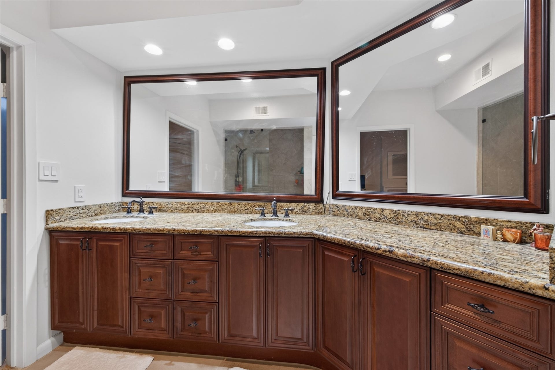 This photo showcases a spacious bathroom with a large granite countertop and dual sinks. It features rich wood cabinetry and two sizable mirrors, creating a luxurious and functional space.