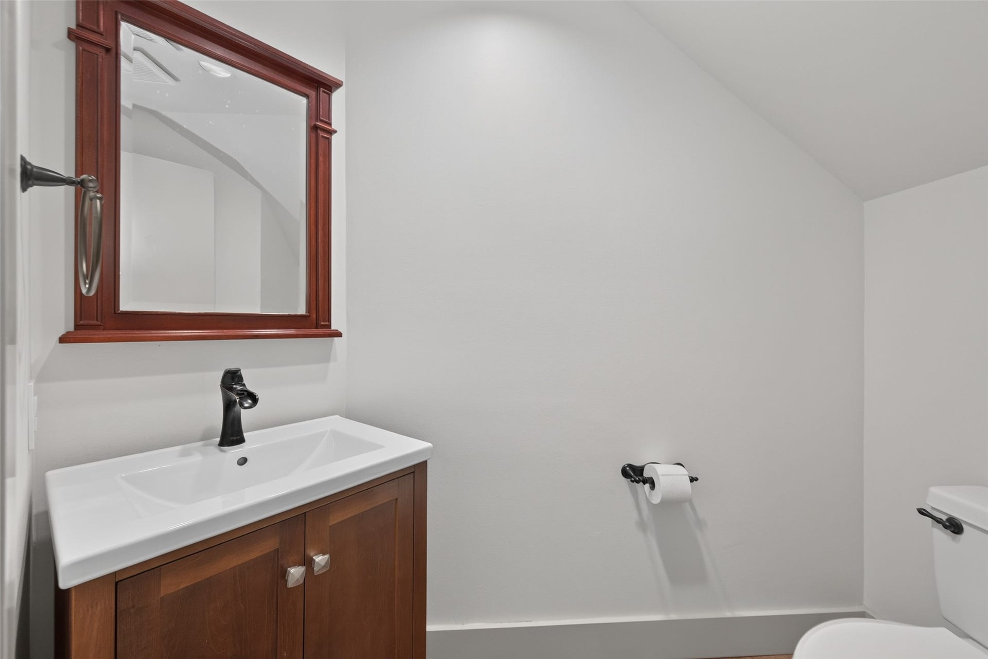 This bathroom features a sleek modern design with a white vanity and dark wood cabinet. It has a black faucet, a large framed mirror, and neutral walls, creating a clean and stylish look.