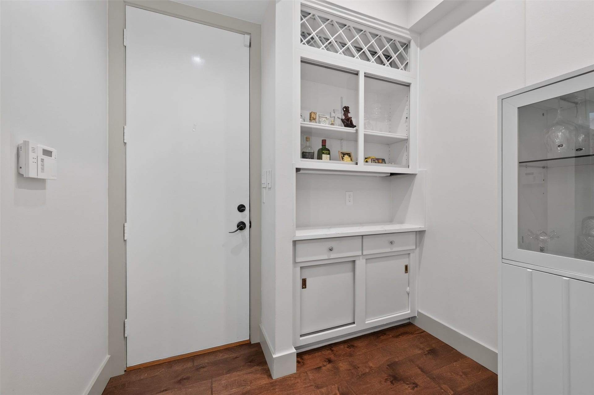 This photo shows a bright, compact entryway featuring a white door and built-in cabinetry with shelving for storage or display, set against polished wood flooring.