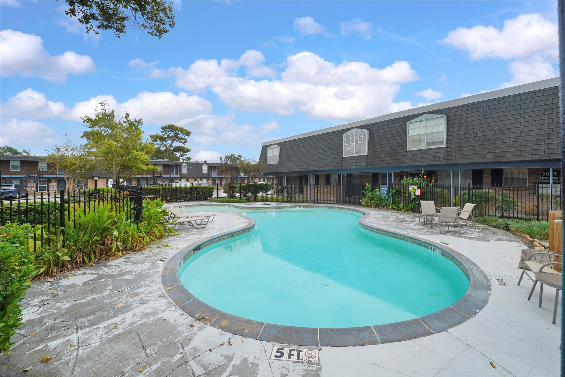 Alternate view of the sparkling swimming pool surrounded by seating and well-maintained property grounds.