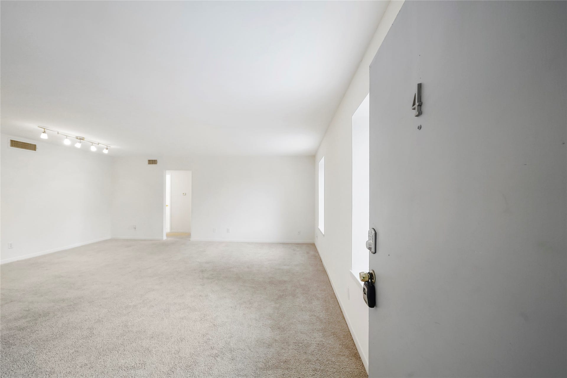 Welcome home view looking into the wide open living area directly from the front entrance, featuring fresh neutral paint, plush carpet, and overhead track lighting.