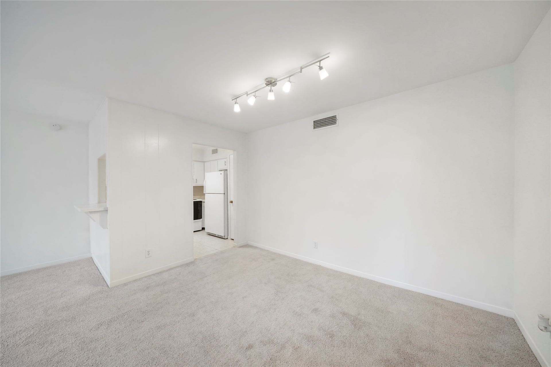 Dedicated dining or multi-purpose living area complete with neutral plush carpeting, modern overhead track lighting, and convenient pass-through counter access.