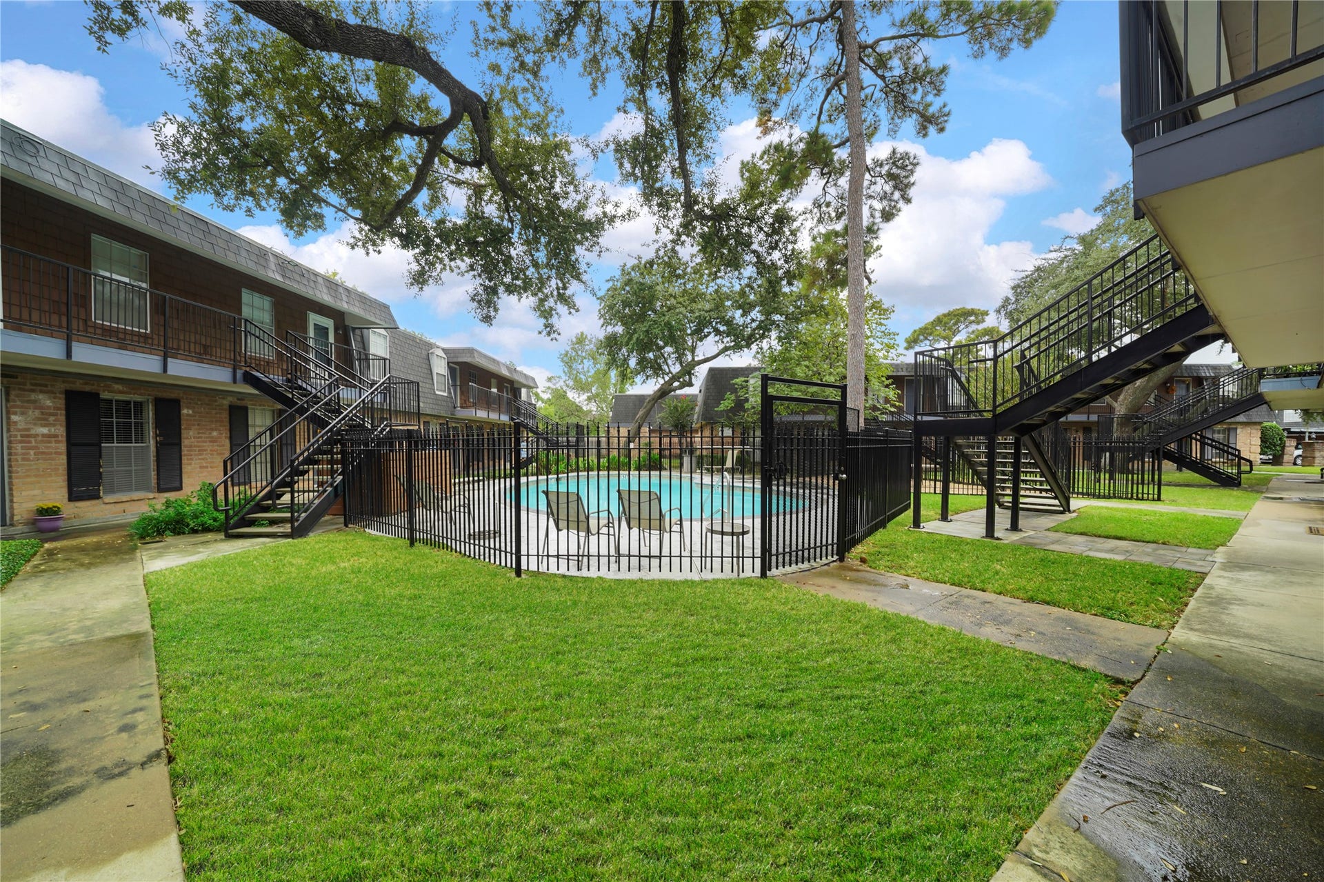Courtyard grounds showing secure wrought-iron fencing around the community pool, surrounded by leafy trees and grassy lawn space.