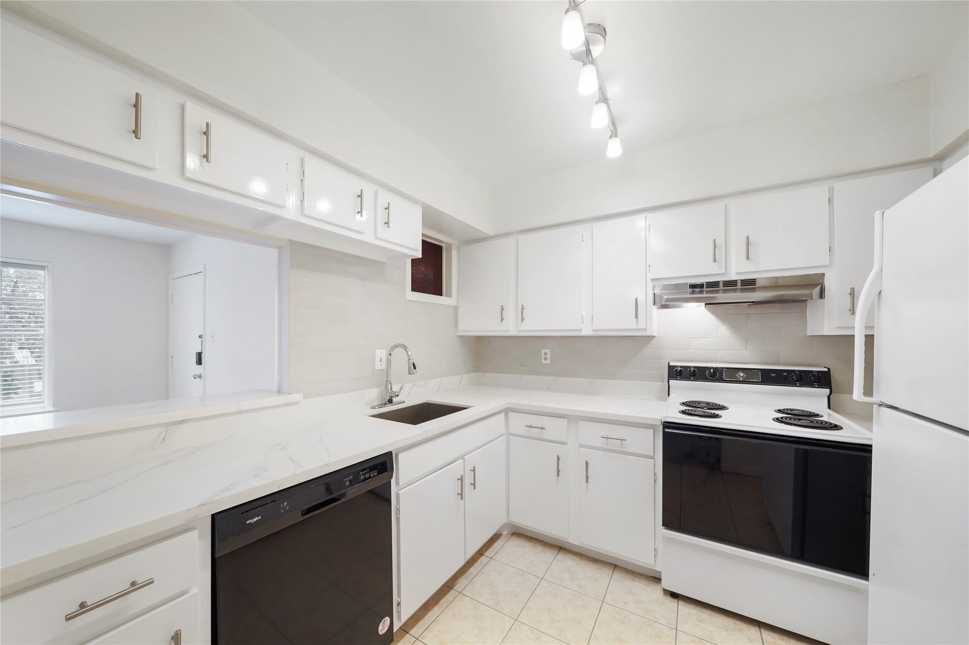 Kitchen highlight showcasing modern white cabinets, clean line counters, electric range, dishwasher, and pass-through counter to the dining room.