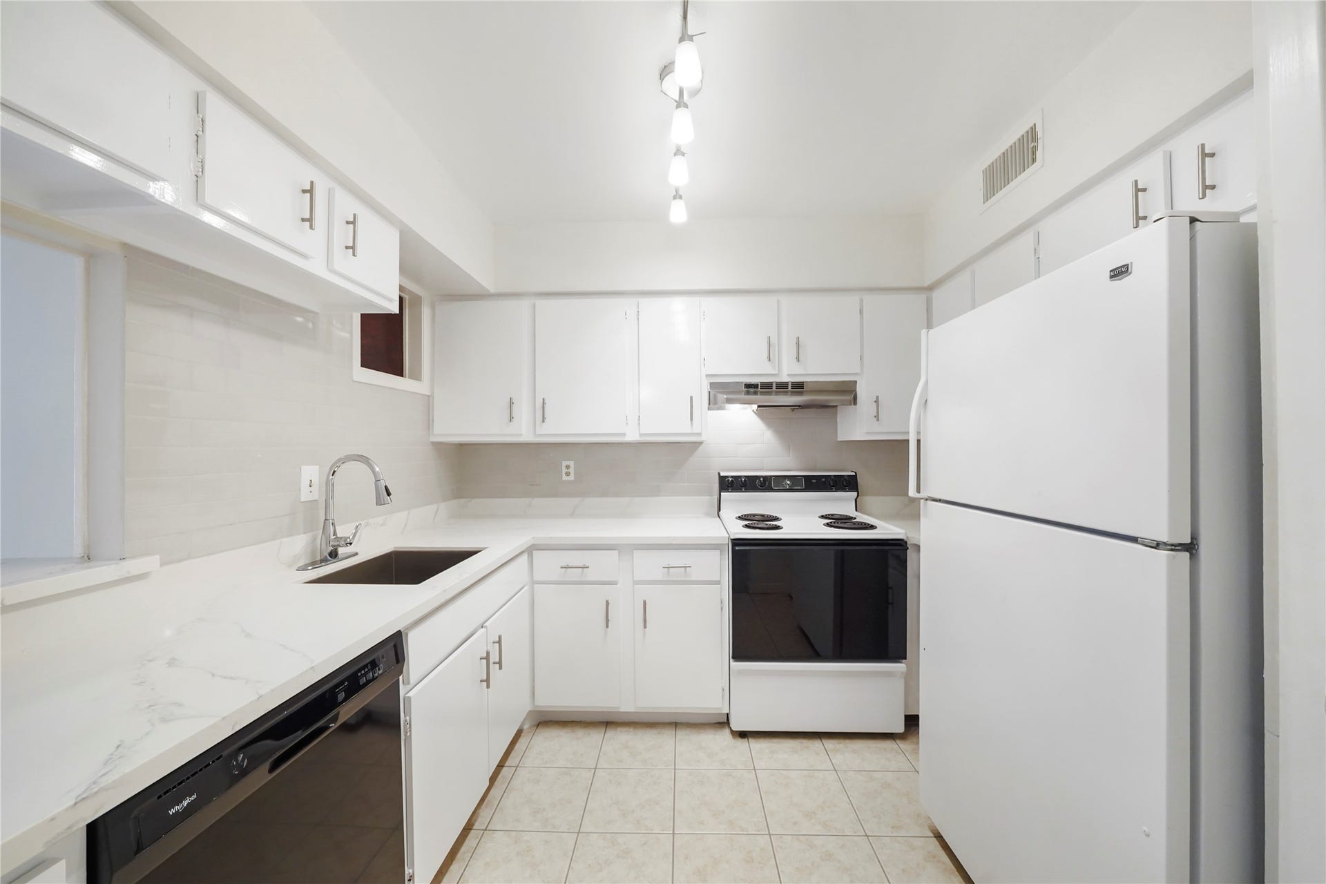 Bright kitchen featuring sleek white cabinetry, crisp countertops, black appliances, a double sink with gooseneck faucet, and easy-care tile flooring.