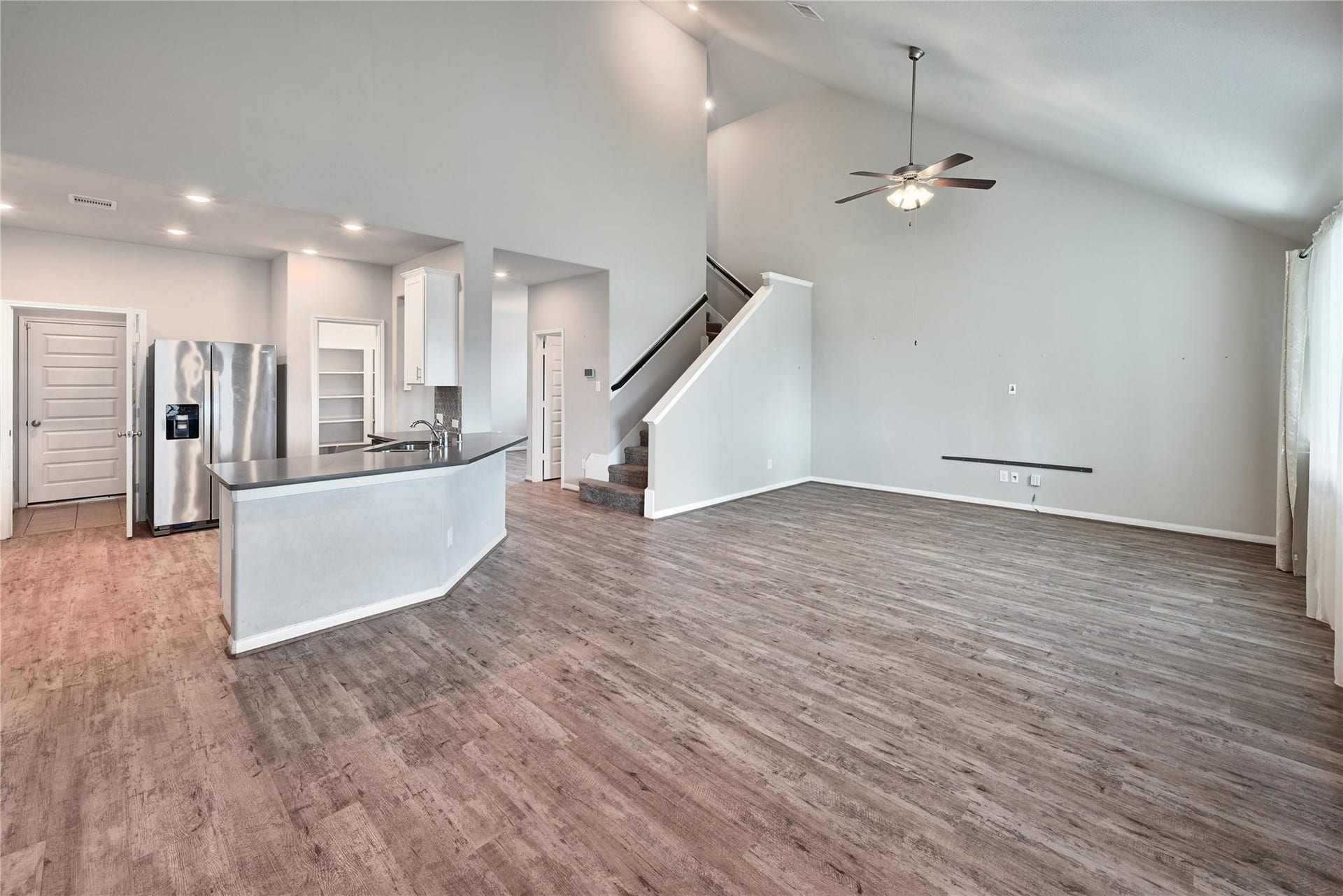 5936 Pearland Place, Pearland, TX 77581 This photo showcases a spacious open-concept living area with high ceilings, modern wood flooring, and abundant natural light. The kitchen features stainless steel appliances and a sleek design. A staircase leads to an upper level, enhancing the home's modern feel.