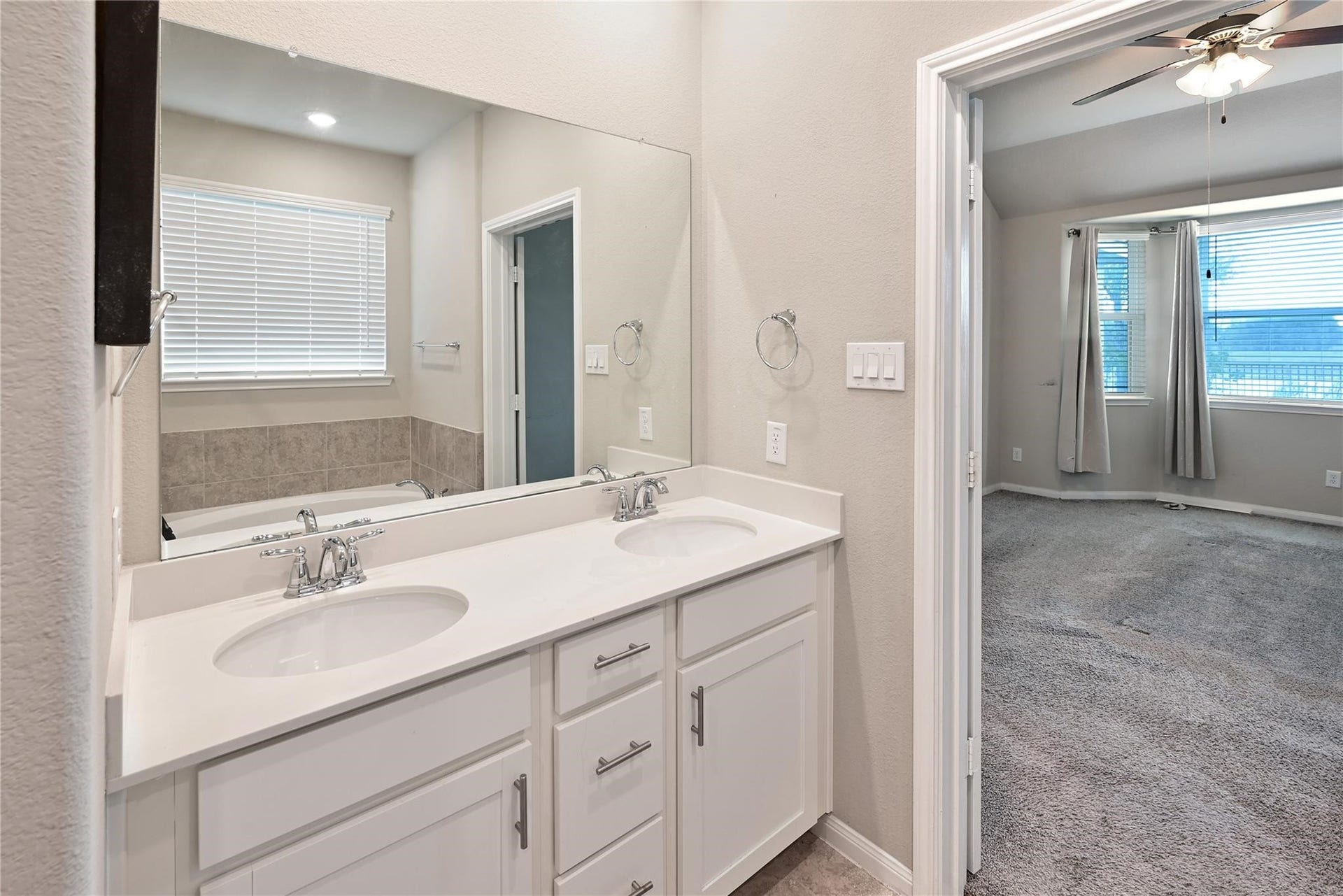 5936 Pearland Place, Pearland, TX 77581 This photo shows a modern bathroom with dual sinks and white cabinetry, adjacent to a carpeted bedroom with large windows and natural light.