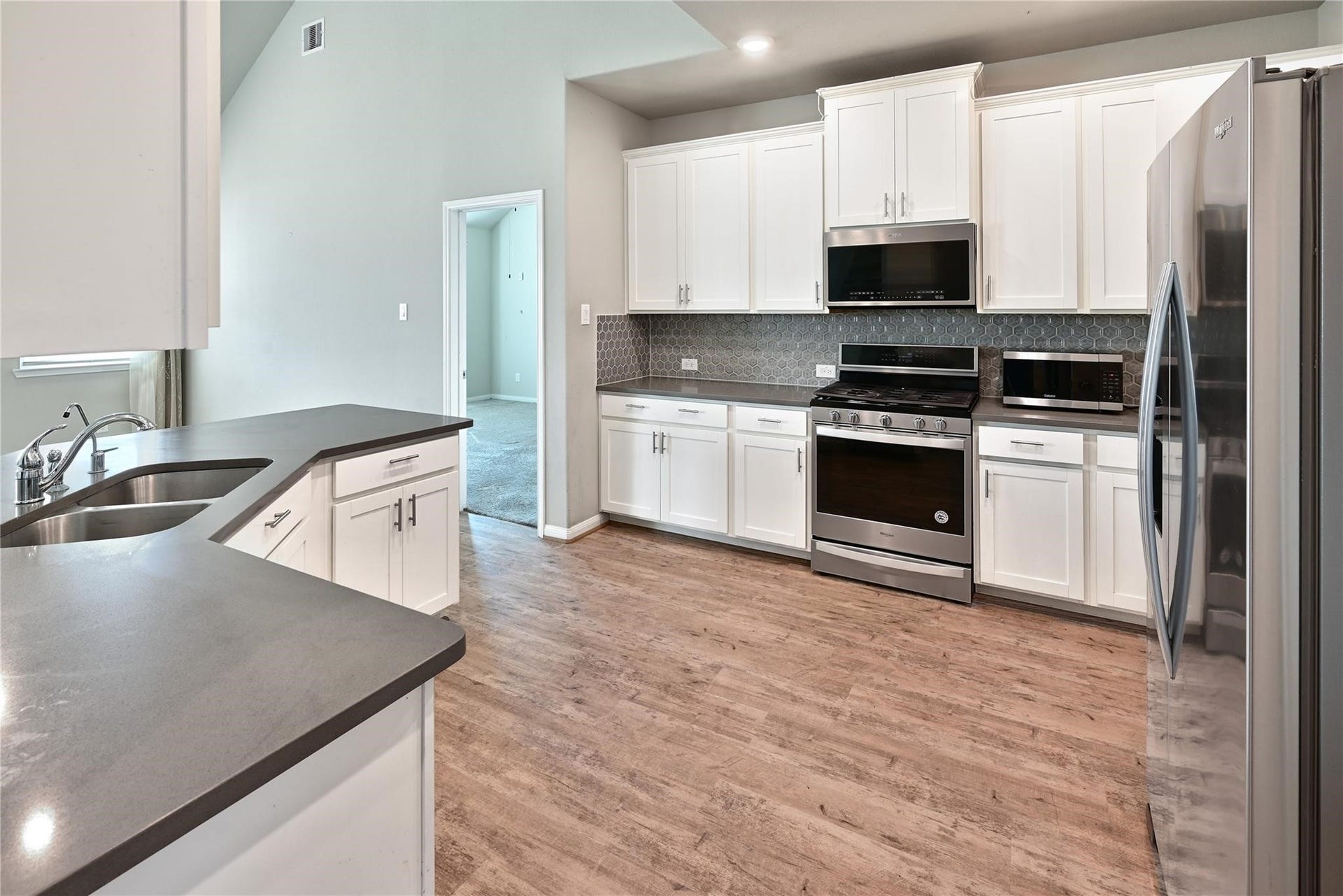 5936 Pearland Place, Pearland, TX 77581 This kitchen features modern stainless steel appliances, white cabinetry, and a sleek, dark countertop. The open layout offers ample space with a view into an adjoining room, and the wood-style flooring adds warmth.