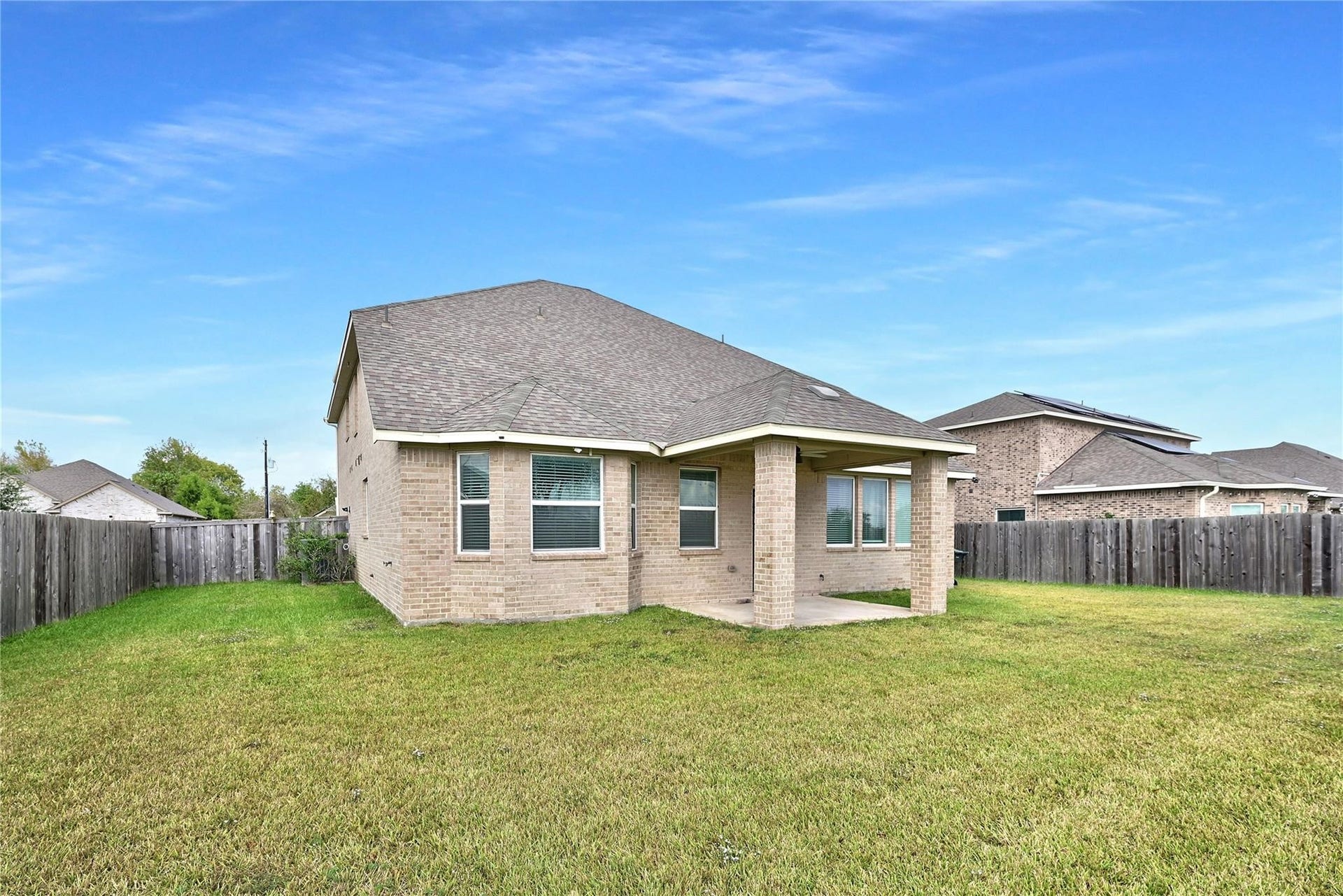 5936 Pearland Place, Pearland, TX 77581 This photo shows a covered patio with brick columns, overlooking a spacious backyard. The area is grassy and fenced, offering a view of a serene pond with a fountain and surrounding greenery, perfect for relaxation and outdoor enjoyment.