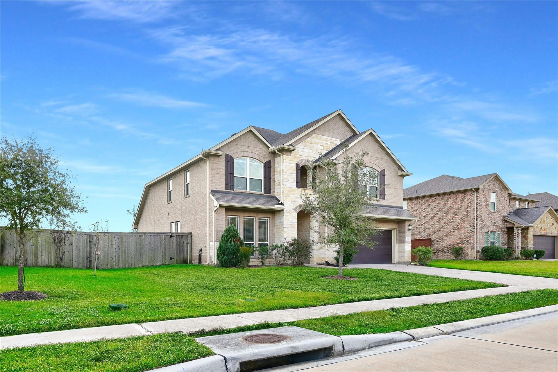5936 Pearland Place, Pearland, TX 77581 This is a two-story brick home with a stone facade, featuring a well-maintained lawn and young trees. It includes a two-car garage and is situated on a corner lot in a suburban neighborhood.