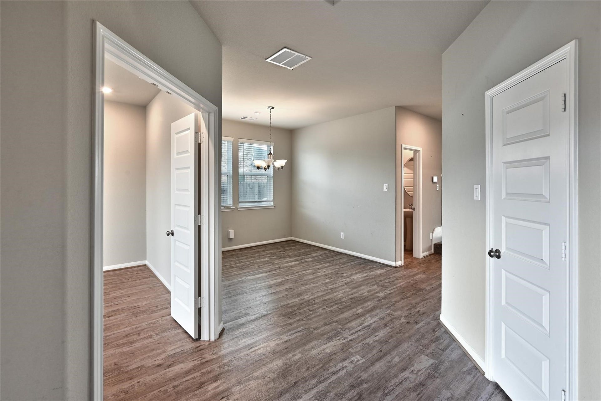 5936 Pearland Place, Pearland, TX 77581 This photo showcases a bright, open space with wood flooring, neutral walls, and white doors. There's a small dining area with a light fixture, adjacent to a hallway leading to a bathroom. Ample natural light enters through a window, enhancing the cozy atmosphere.