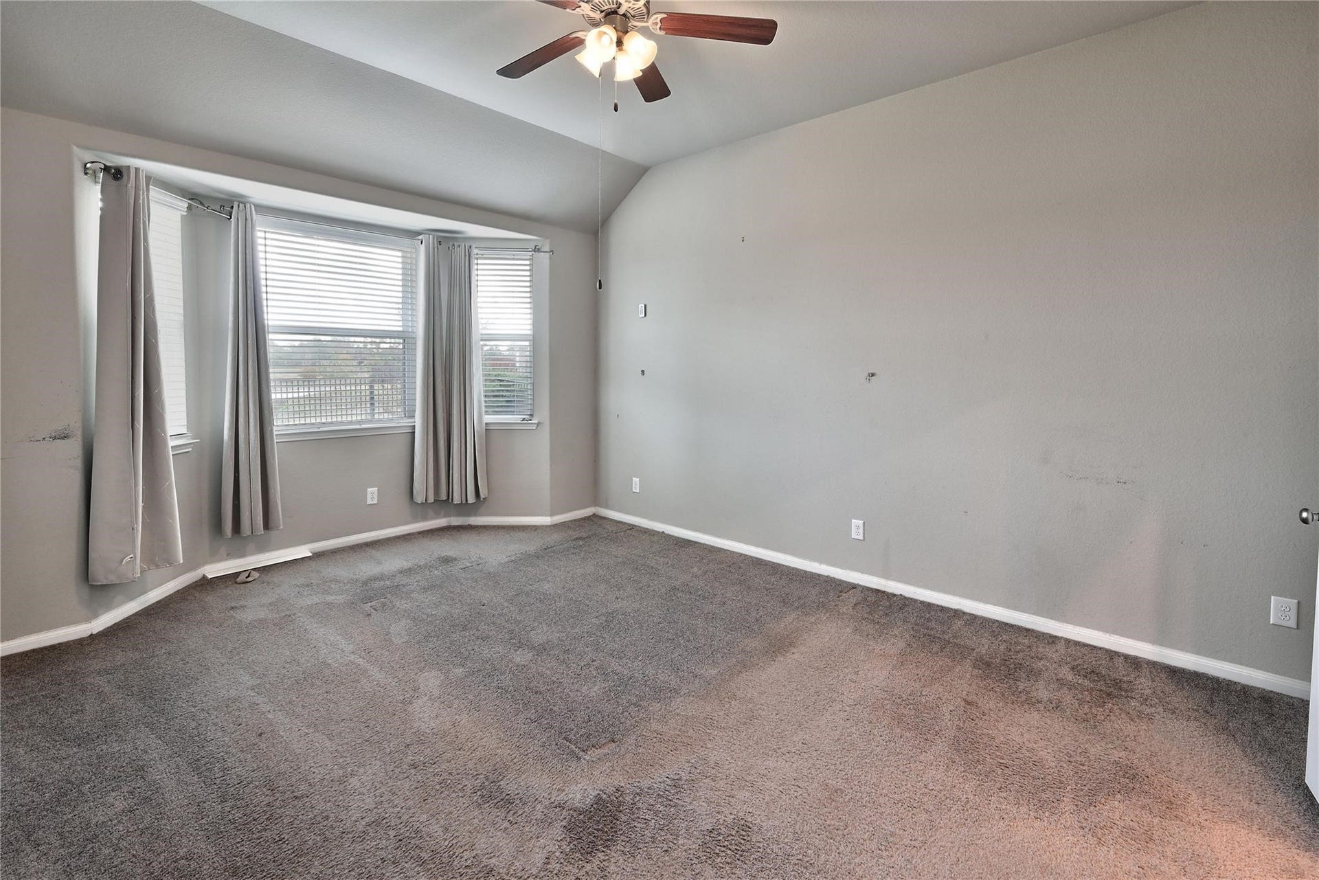 5936 Pearland Place, Pearland, TX 77581 This is a spacious, unfurnished bedroom featuring a vaulted ceiling and a ceiling fan. It has a large bay window with curtains, providing ample natural light. The room is carpeted and has neutral-colored walls.