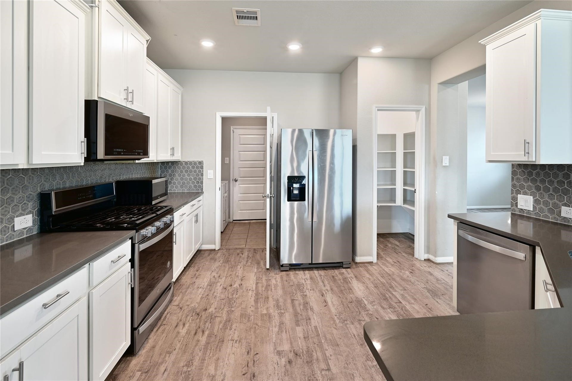 5936 Pearland Place, Pearland, TX 77581 Modern kitchen with white cabinetry, stainless steel appliances, and a sleek hexagonal tile backsplash. The space features wood-style flooring, ample counter space, and a convenient pantry.