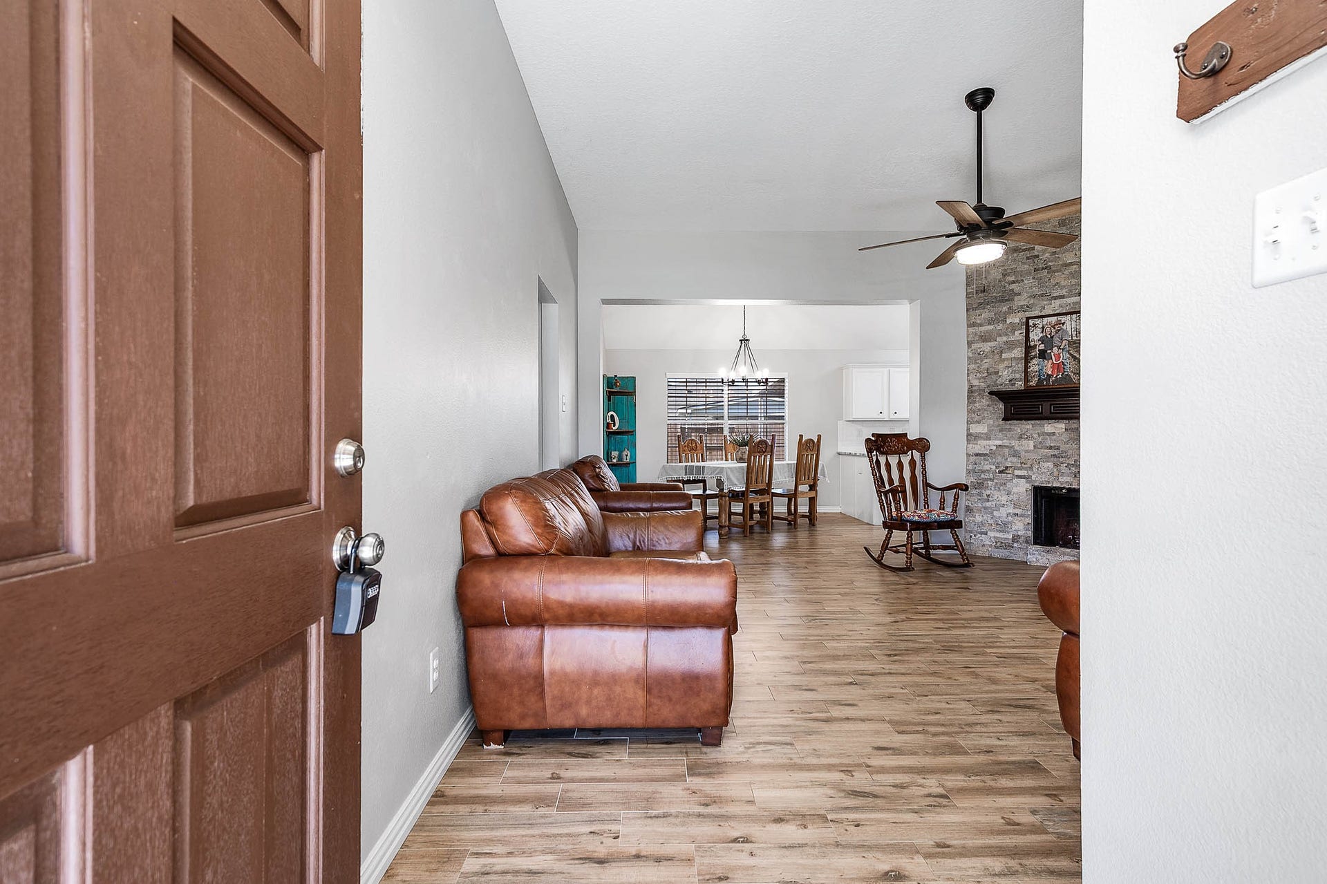 Step into a spacious open living area featuring warm wood floors, a cozy stone fireplace, and a ceiling fan, seamlessly connecting to a dining space with abundant natural light.