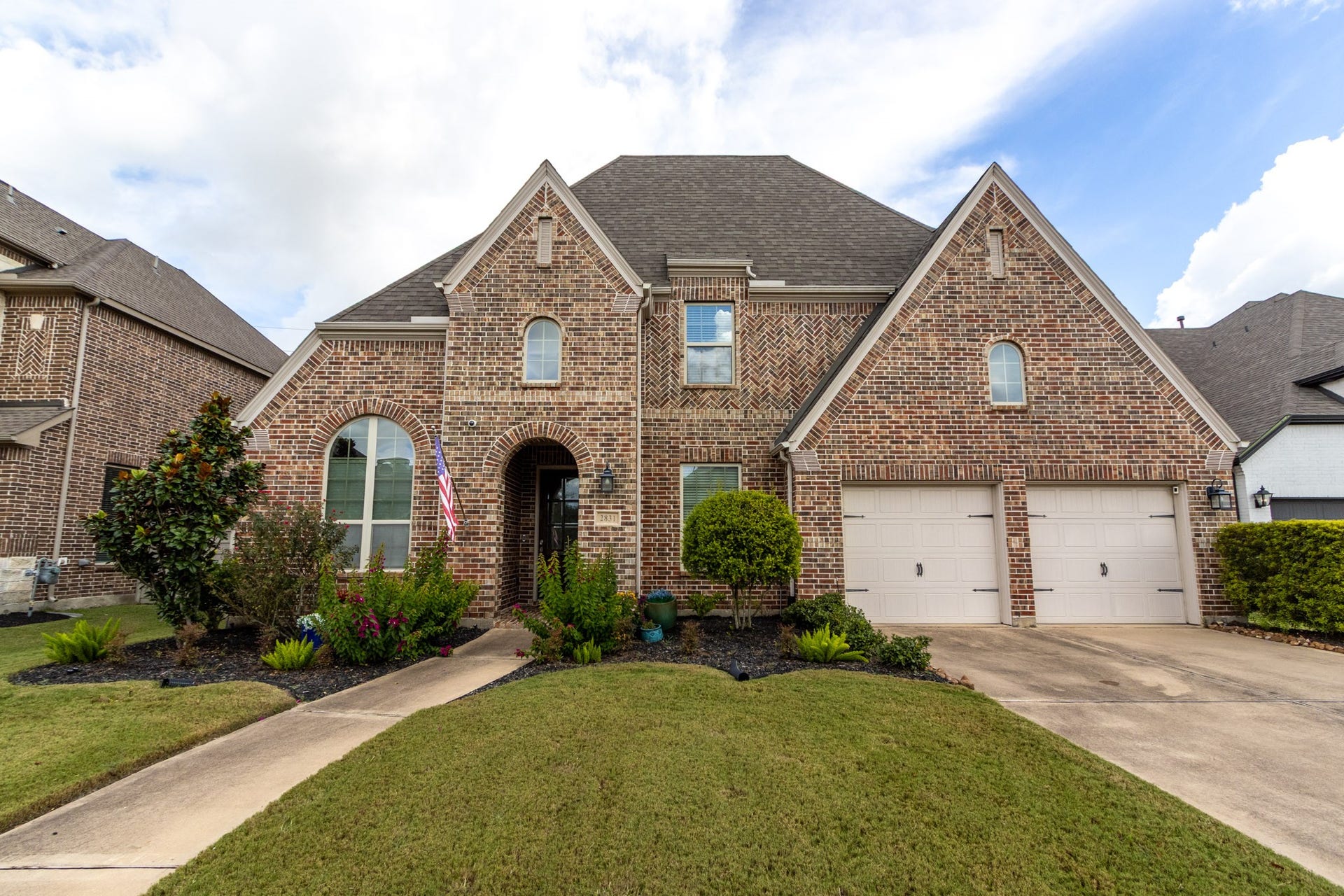 2831 Maple Oak Lane, Manvel, TX 77578 This charming brick home features a classic design with a steep roof and arched windows. It includes a spacious two-car garage, a well-maintained front yard with tasteful landscaping, and a welcoming walkway leading to the entrance.