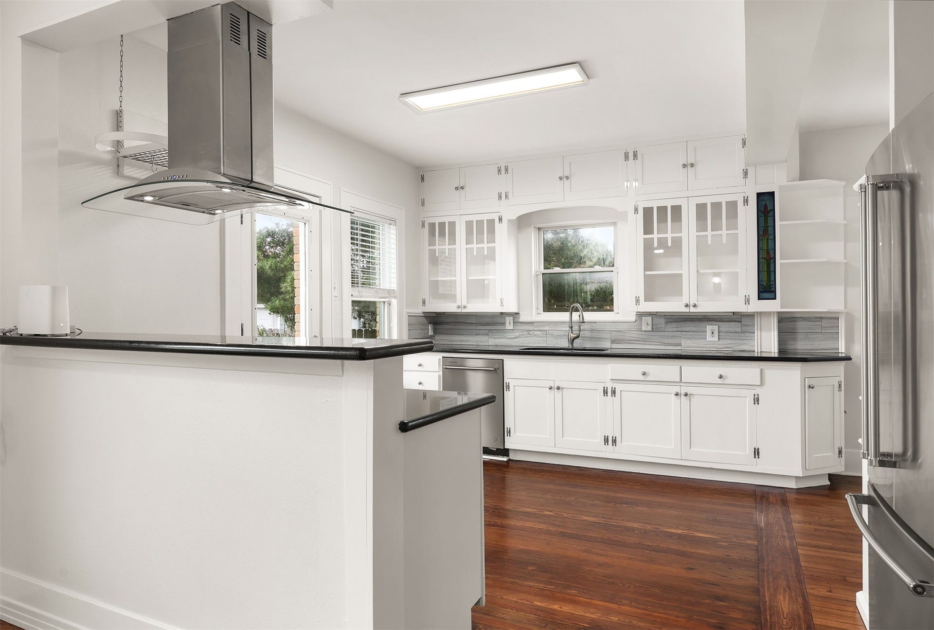 4323 Sherman Boulevard, Galveston, TX 77550 Charming kitchen with white cabinetry, sleek dark countertops, and rich hardwood floors, featuring modern stainless steel appliances.