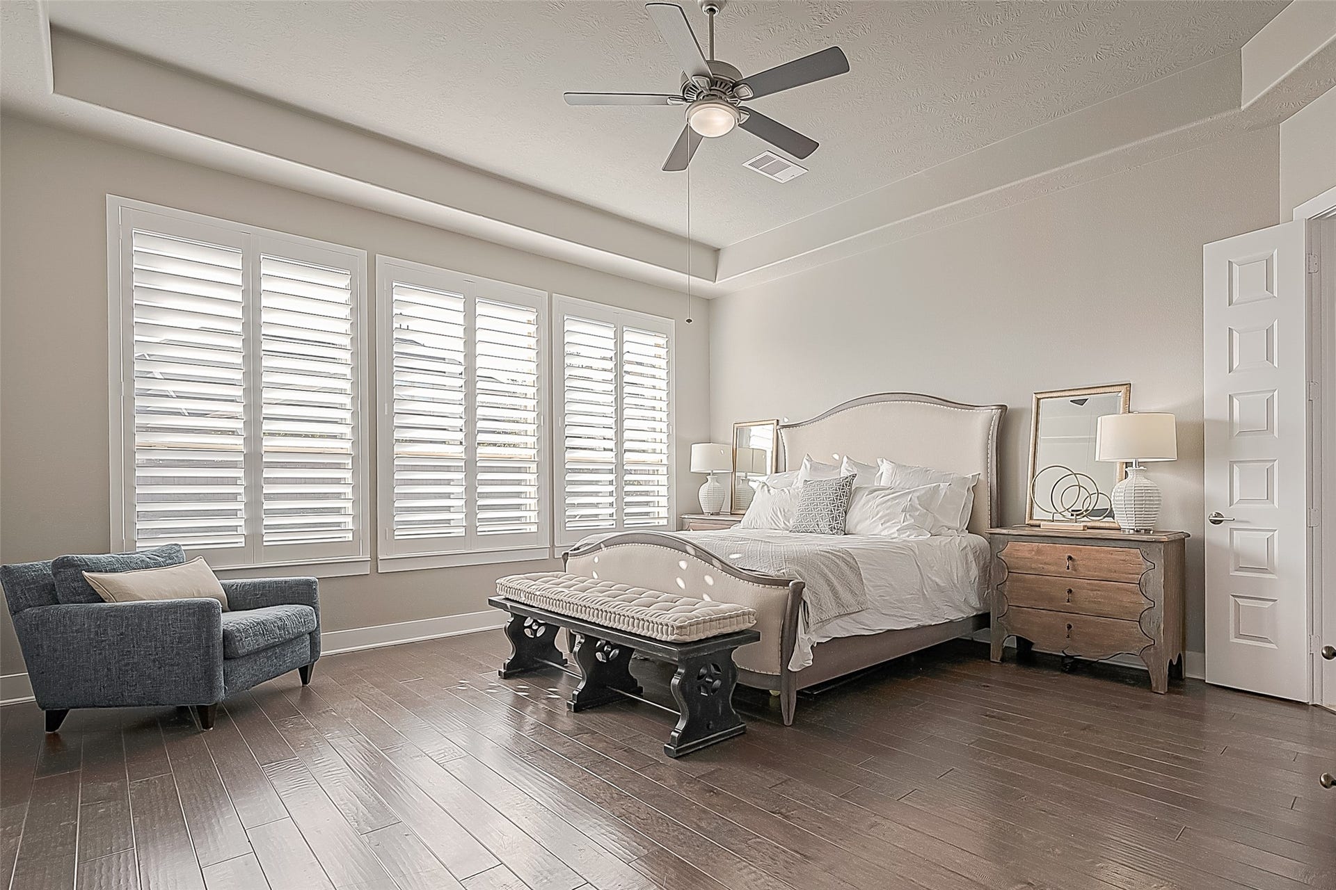 30 Argosy Bend Place, Tomball, TX 77375 The expansive primary bedroom features inviting warm wood flooring, Plantation shutters, a ceiling fan, and ample space for a king bed and additional seating.