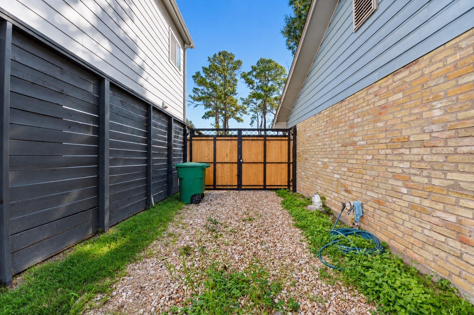 1837 Wycliffe Drive, Houston, TX 77043 Charming side yard with a mix of gravel and grass, featuring a modern black fence and a wooden gate for added privacy.
