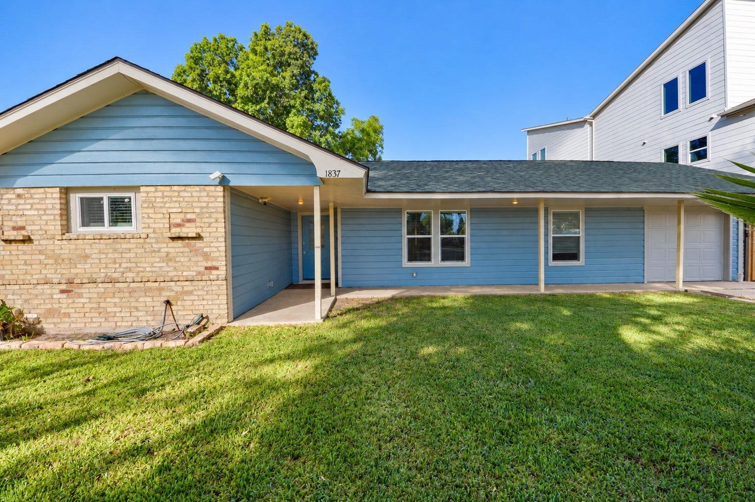 1837 Wycliffe Drive, Houston, TX 77043 Charming single-story home featuring a mix of brick and blue siding, complemented by a lush, well-maintained front lawn and a covered entryway.
