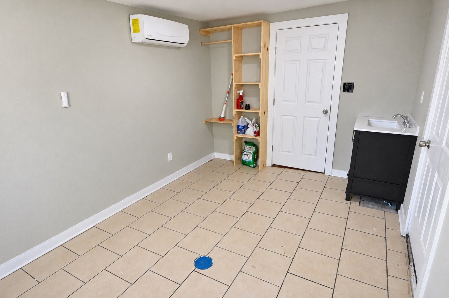 1837 Wycliffe Drive, Houston, TX 77043 Spacious utility room with tiled flooring, featuring built-in wooden shelving, a convenient sink, and efficient wall-mounted HVAC unit.