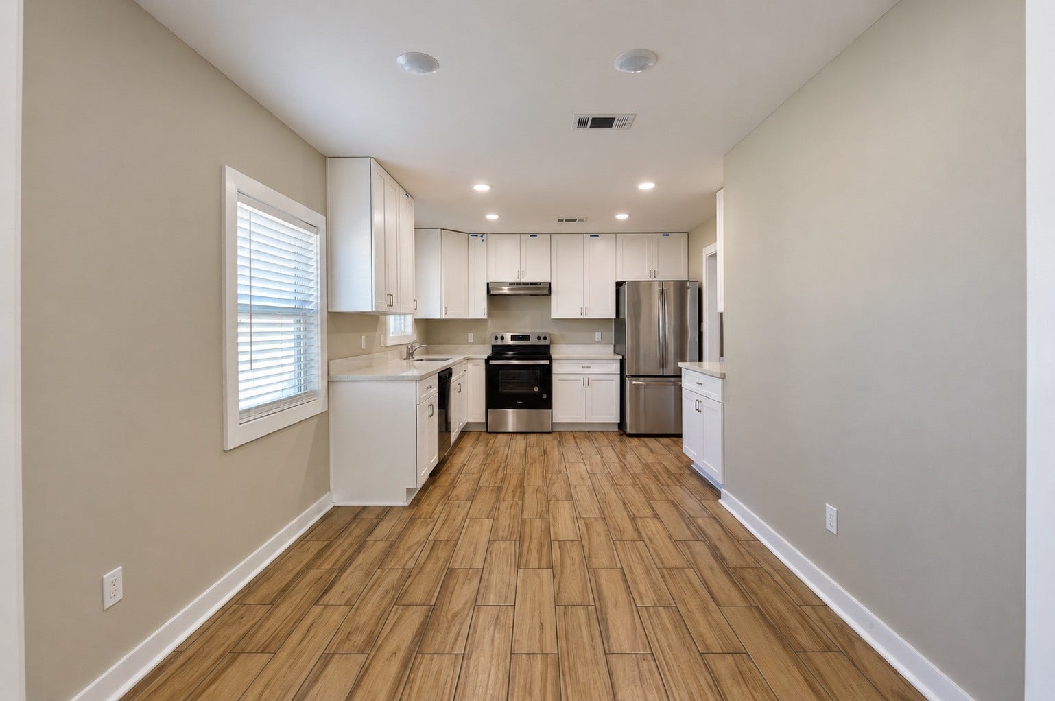 1837 Wycliffe Drive, Houston, TX 77043 Sleek kitchen with modern stainless steel appliances, elegant white cabinetry, and warm wood-look tile flooring, offering a bright and inviting space for culinary creativity.