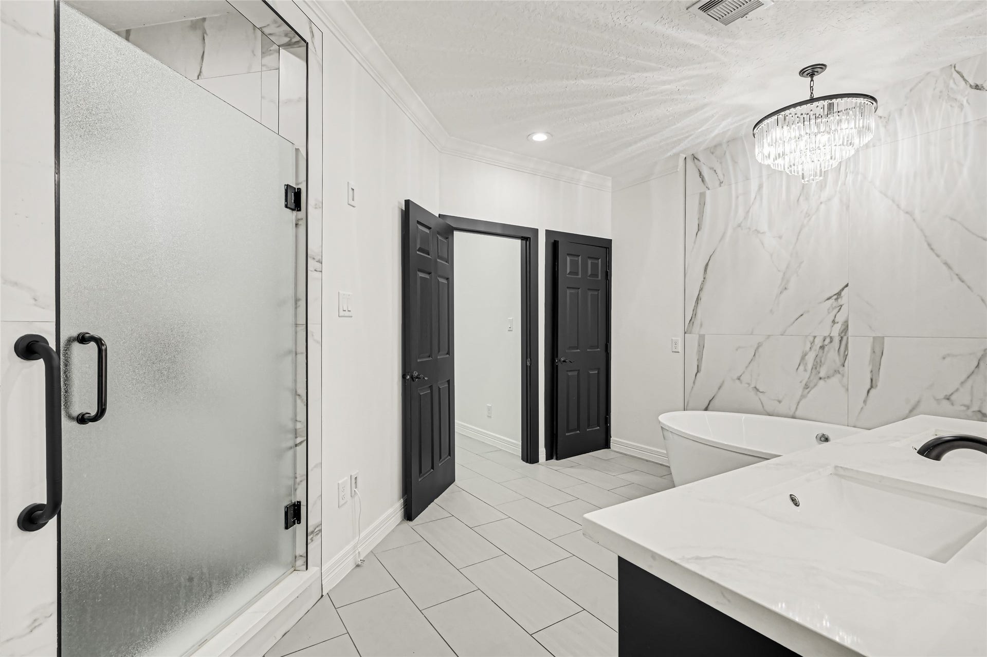 19763 Irenell Dr, Porter, TX 77365 Elegant bathroom featuring a luxurious marble design, a sleek glass shower, and a stylish freestanding tub under a stunning chandelier.