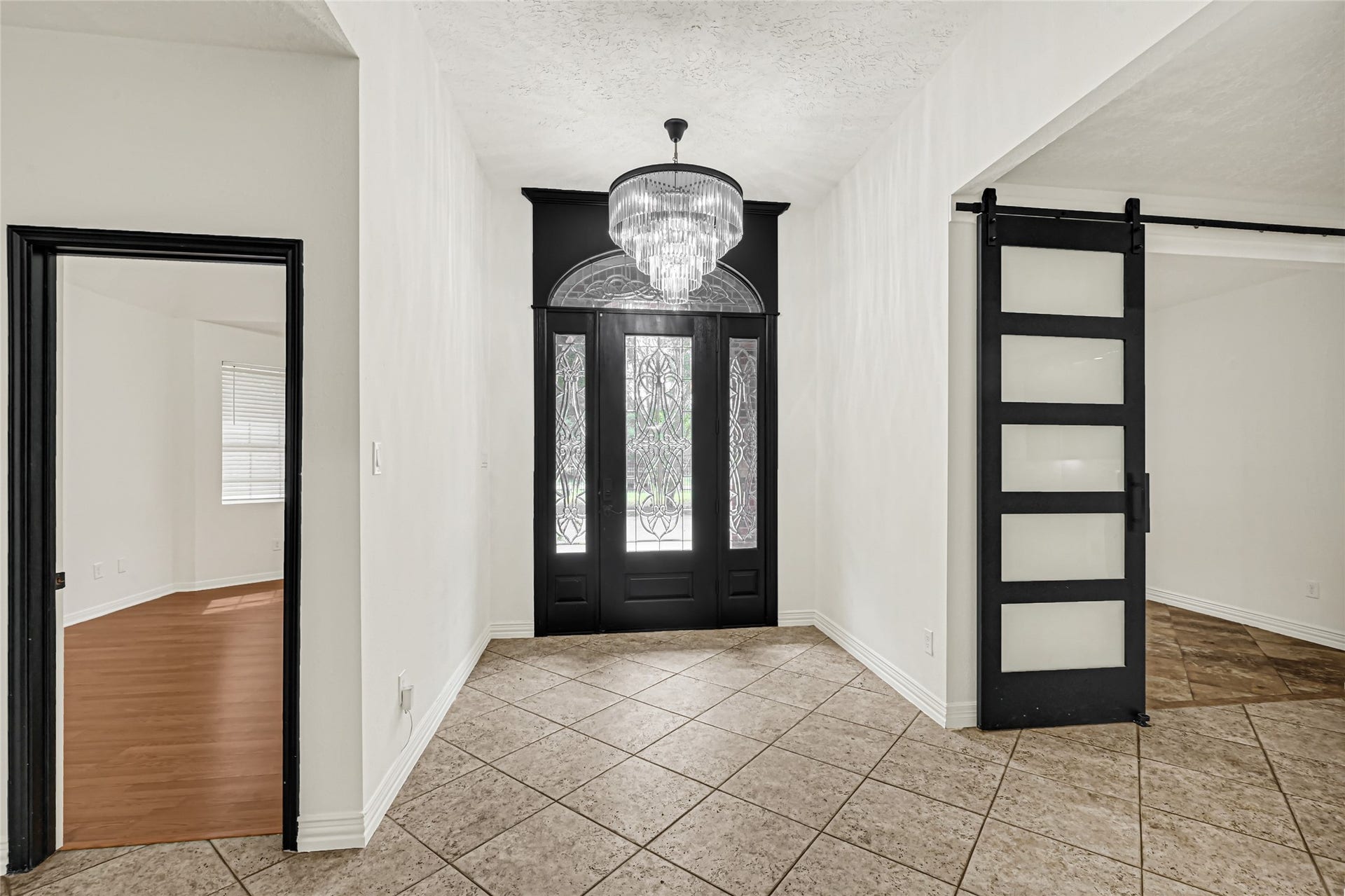 19763 Irenell Dr, Porter, TX 77365 Elegant entryway featuring a stunning chandelier, intricate glass double doors, and modern sliding door with frosted panels, complemented by stylish tile flooring.