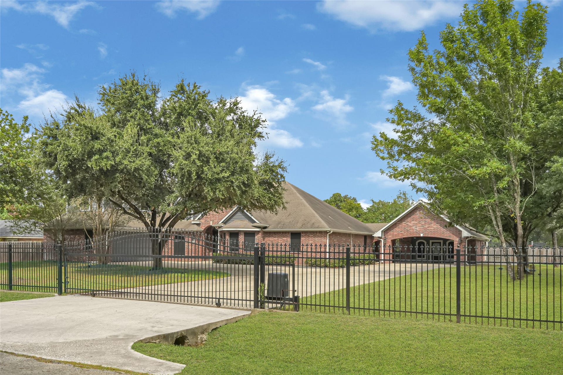 19763 Irenell Dr, Porter, TX 77365 Charming brick home with a spacious front yard, gated driveway, and mature trees providing ample shade.