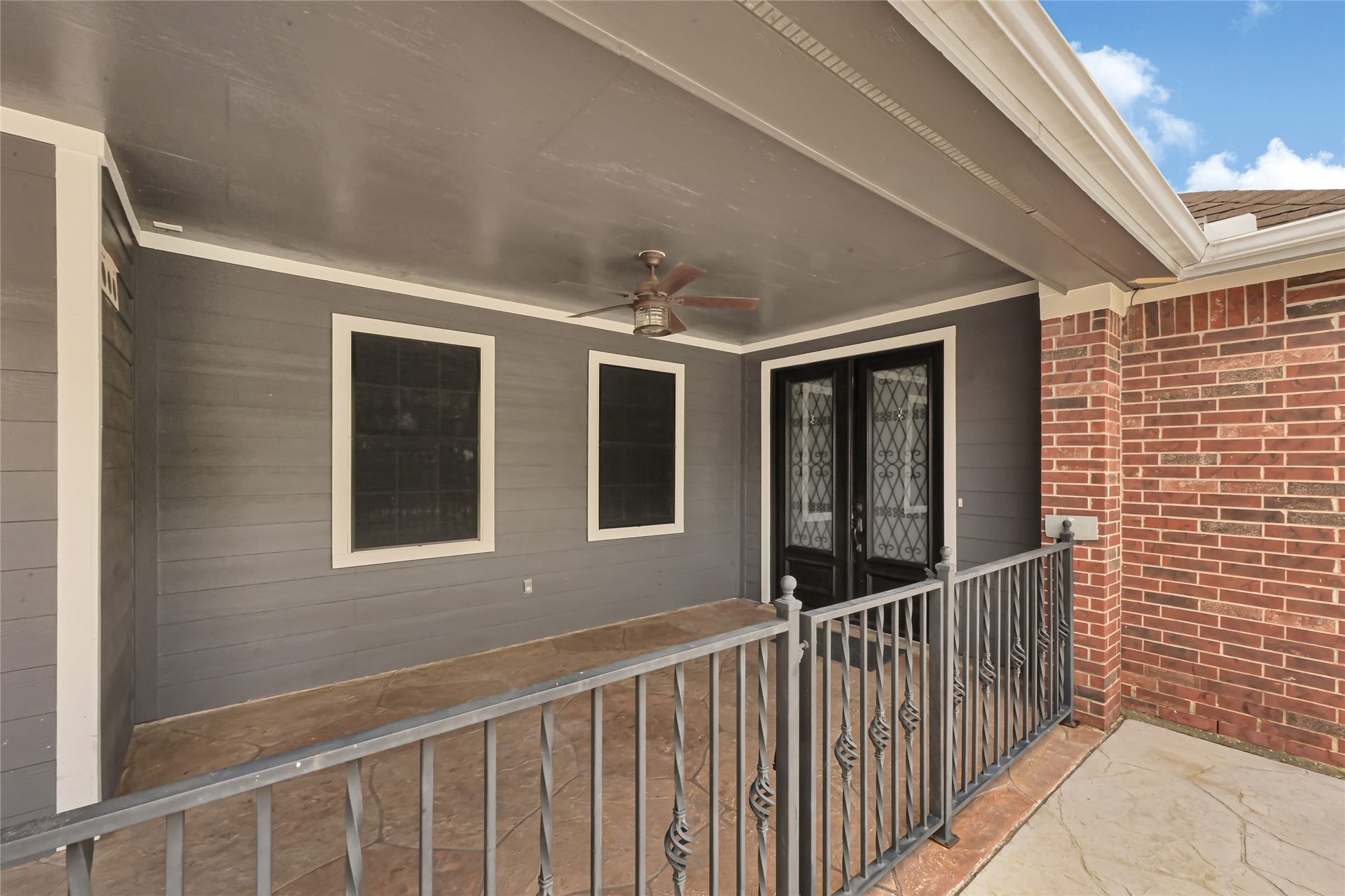 19763 Irenell Dr, Porter, TX 77365 Charming covered patio with elegant wrought iron railing, ceiling fan, and stylish double doors, perfect for relaxing outdoors.