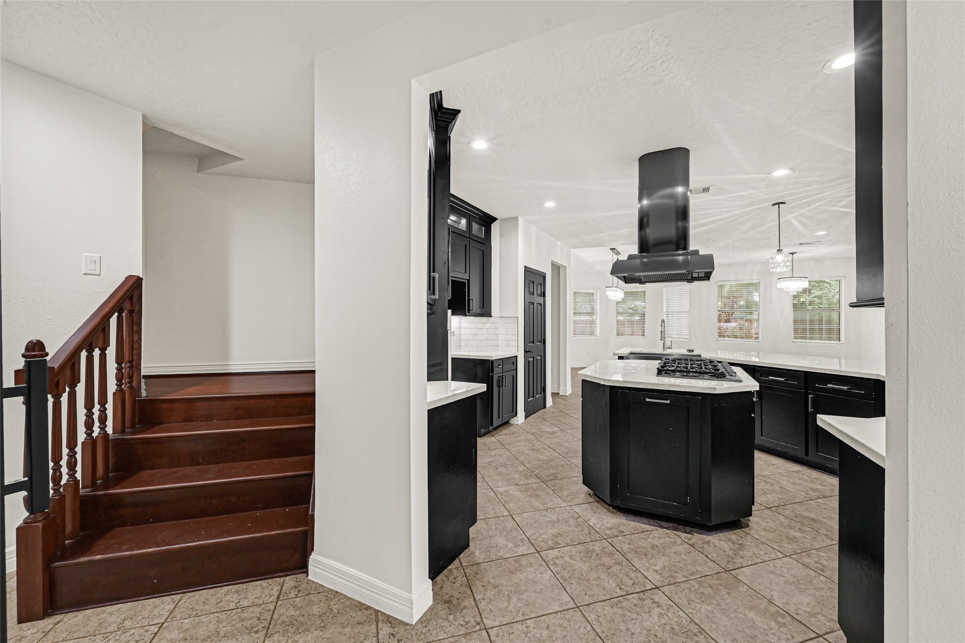 19763 Irenell Dr, Porter, TX 77365 Modern kitchen with sleek black cabinetry, a central island with a cooktop, and bright recessed lighting, adjacent to a warm wooden staircase.