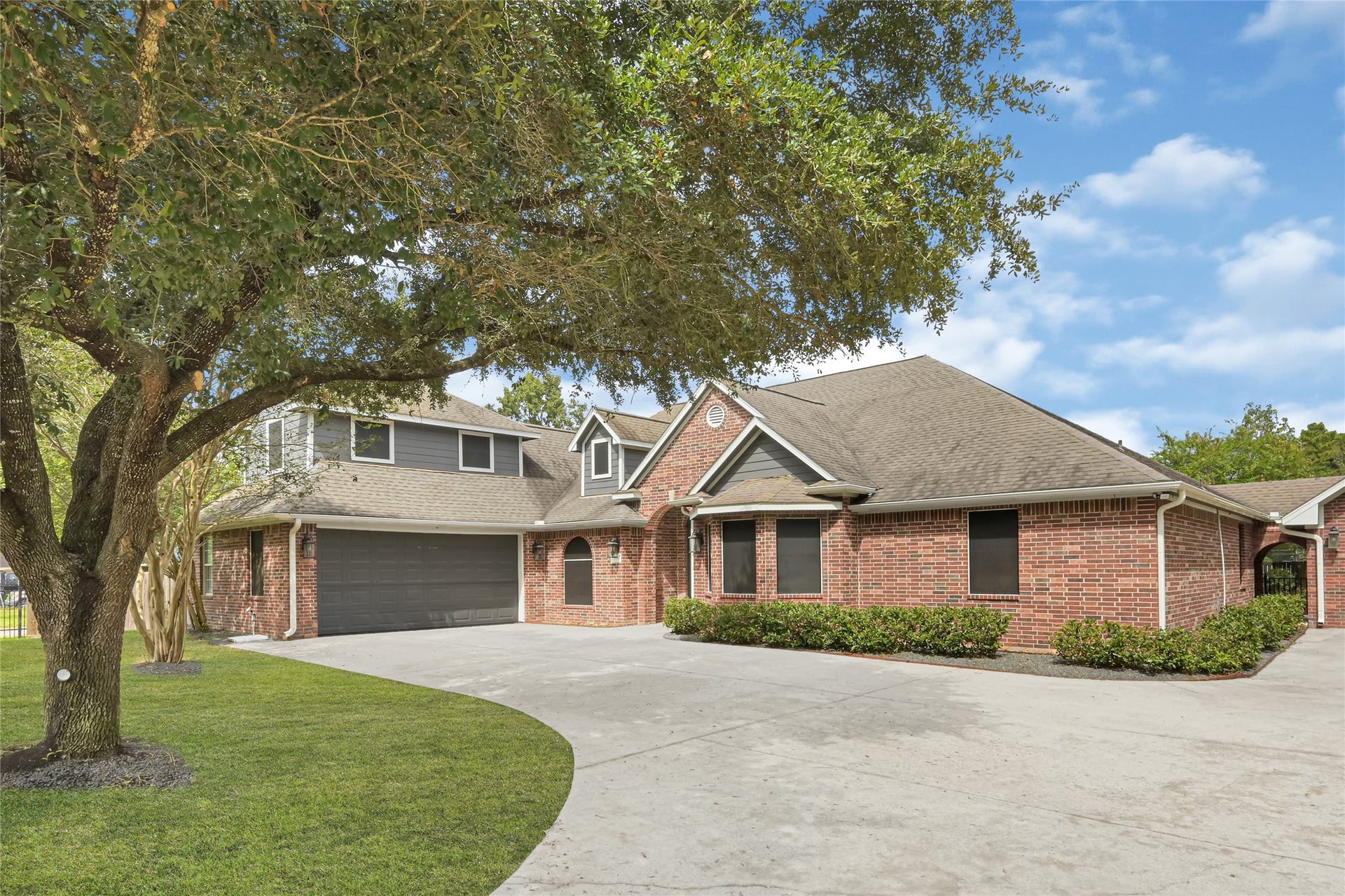 19763 Irenell Dr, Porter, TX 77365 Charming brick home with a spacious driveway and a two-car garage, nestled under mature trees for added shade and privacy.
