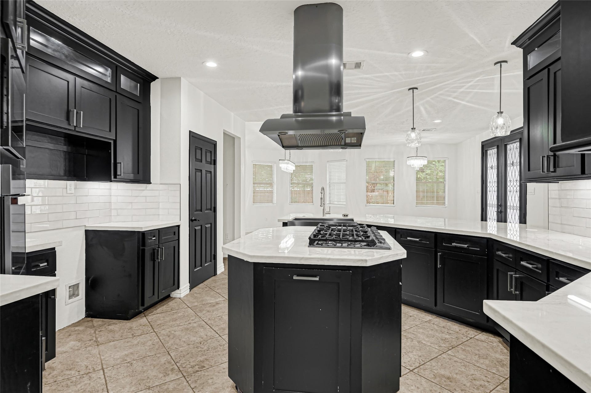 19763 Irenell Dr, Porter, TX 77365 Sleek modern kitchen featuring black cabinetry, a central island with a gas cooktop, and elegant pendant lighting, complemented by white subway tile backsplash and ample natural light.