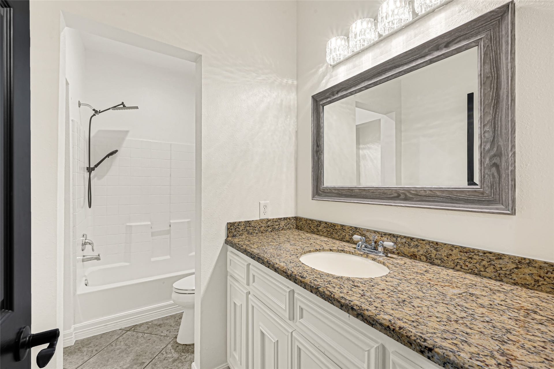 19763 Irenell Dr, Porter, TX 77365 Elegant bathroom featuring a granite countertop with ample storage, a large framed mirror, and a well-appointed shower-tub combination.