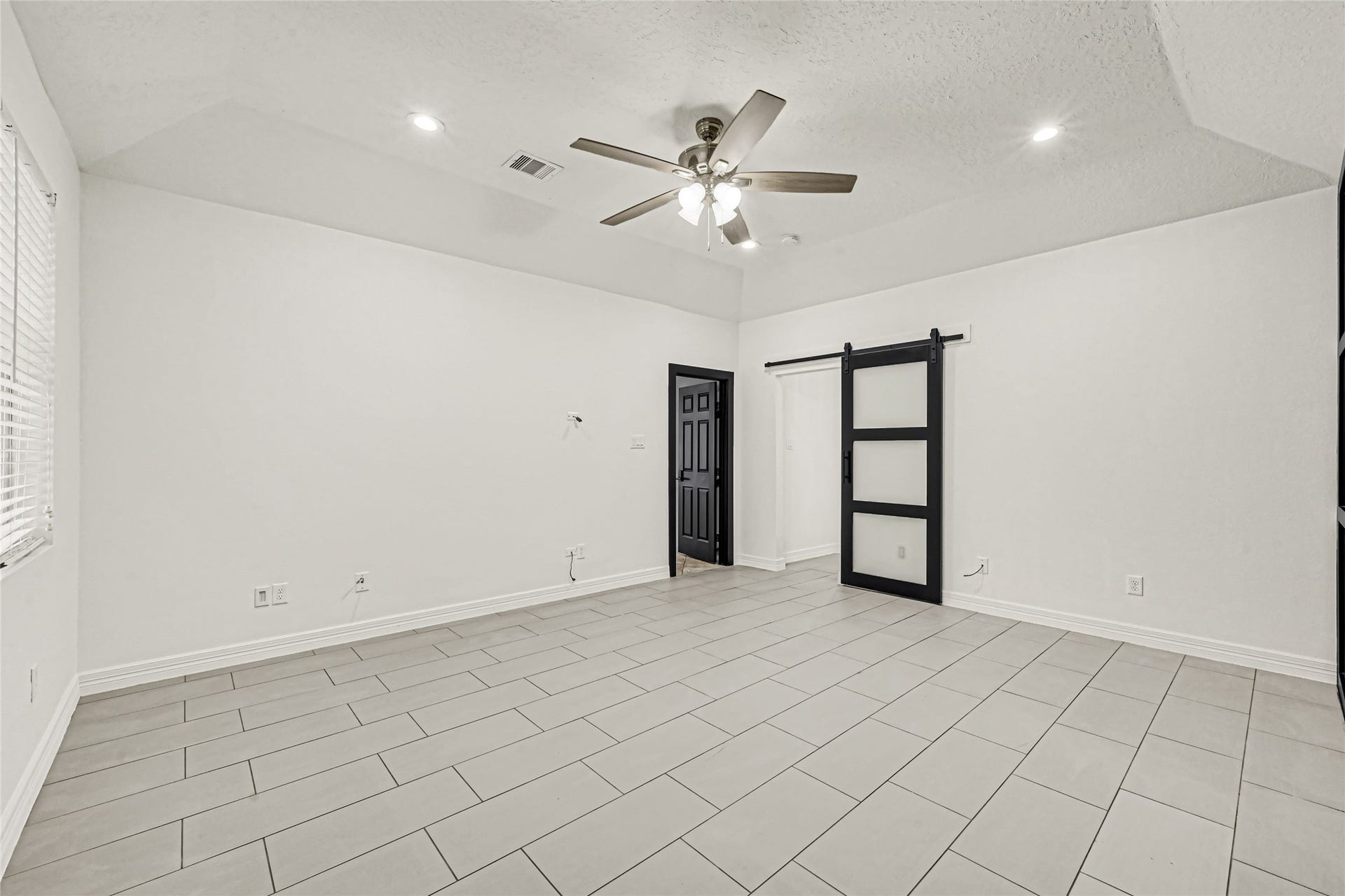 19763 Irenell Dr, Porter, TX 77365 Spacious room featuring sleek tile flooring, a modern ceiling fan, and a stylish barn door for a contemporary touch.