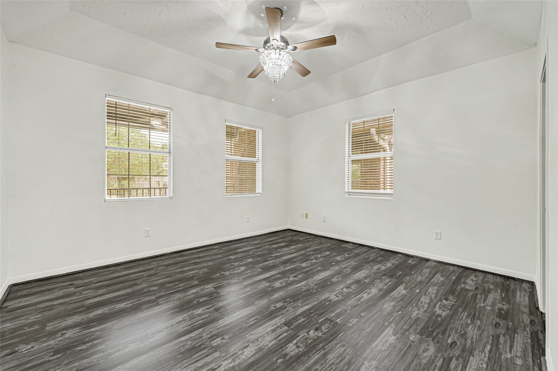 19763 Irenell Dr, Porter, TX 77365 Spacious room with elegant dark wood flooring, abundant natural light from three windows, and a stylish ceiling fan with a chandelier accent.