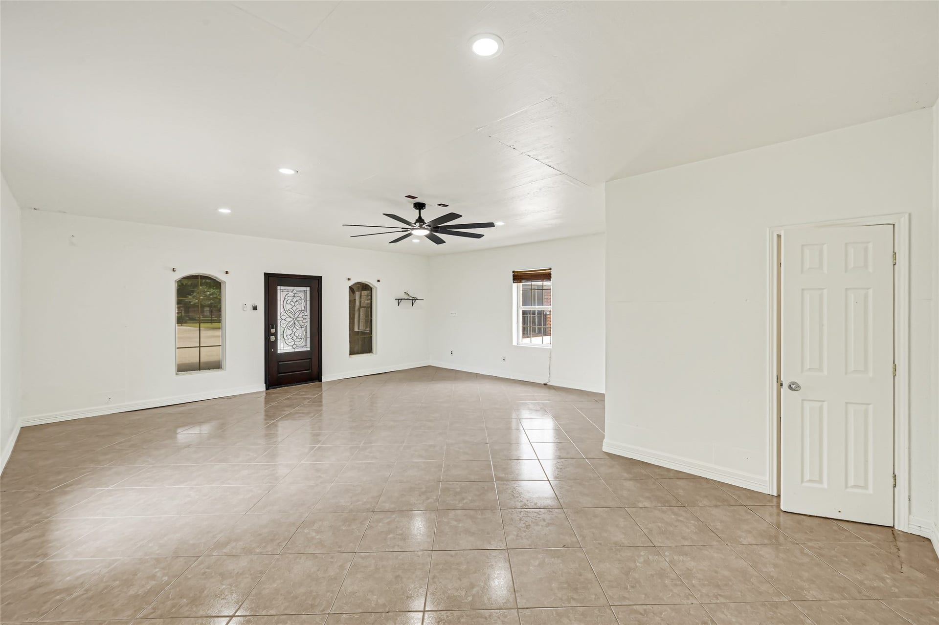 19763 Irenell Dr, Porter, TX 77365 Spacious living area with elegant tiled flooring, bright walls, and a stylish ceiling fan, featuring a decorative front door and ample natural light from multiple windows.