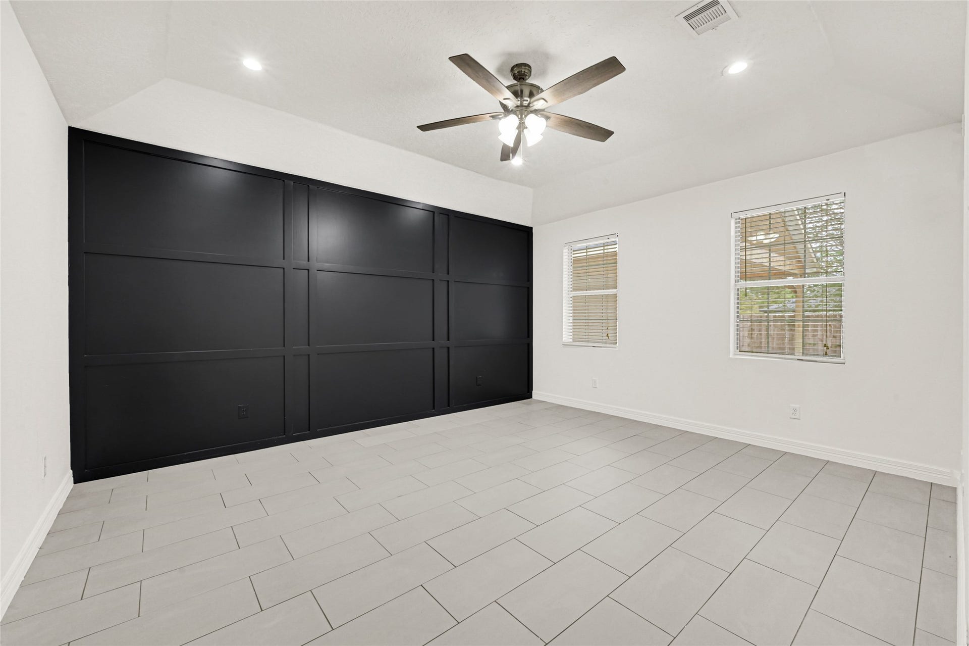19763 Irenell Dr, Porter, TX 77365 Spacious room with sleek black accent wall, modern tile flooring, and ample natural light from dual windows, complemented by a stylish ceiling fan.
