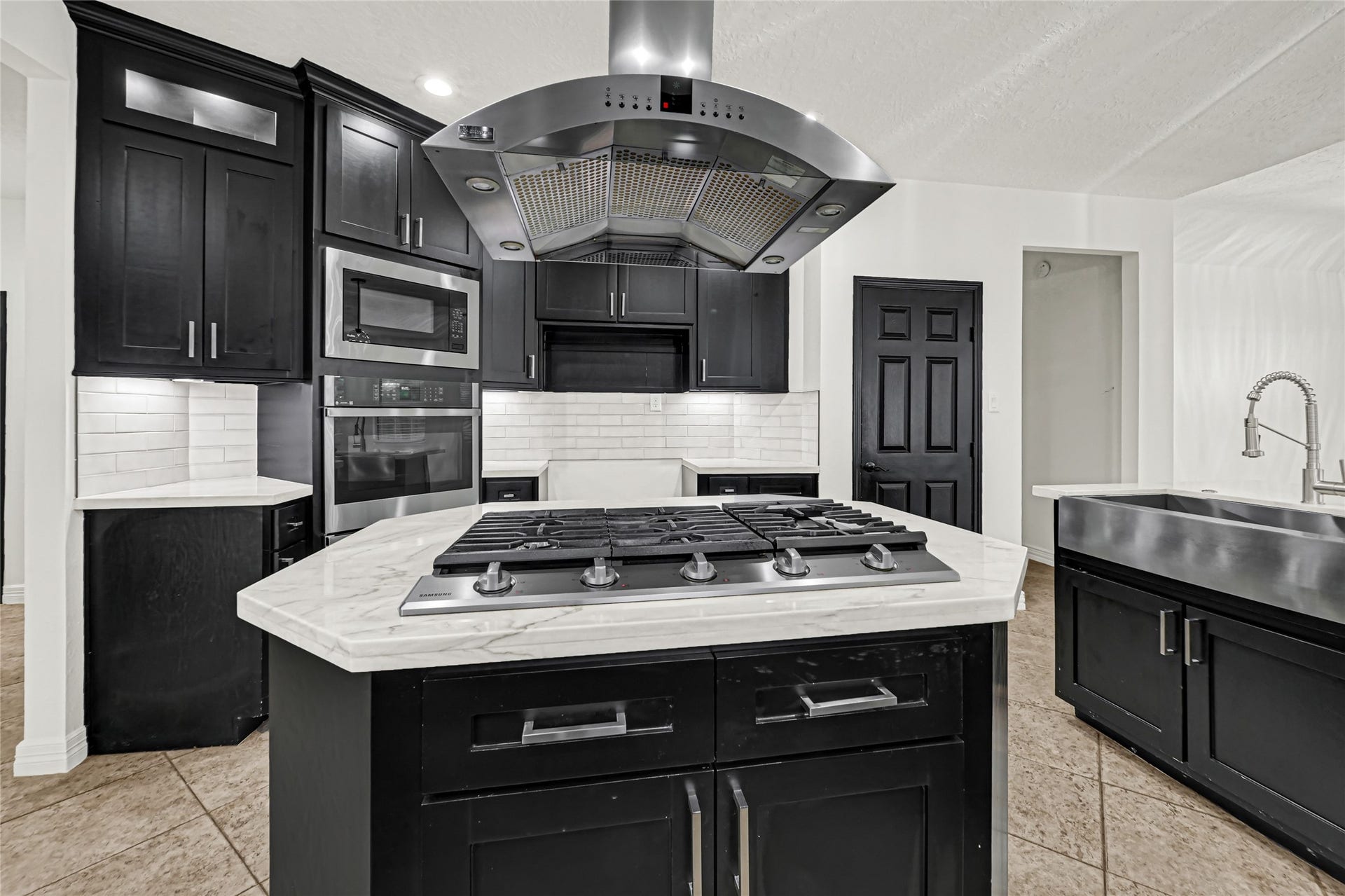 19763 Irenell Dr, Porter, TX 77365 Sleek modern kitchen featuring a central island with a gas cooktop and elegant range hood, surrounded by dark cabinetry and stainless steel appliances.