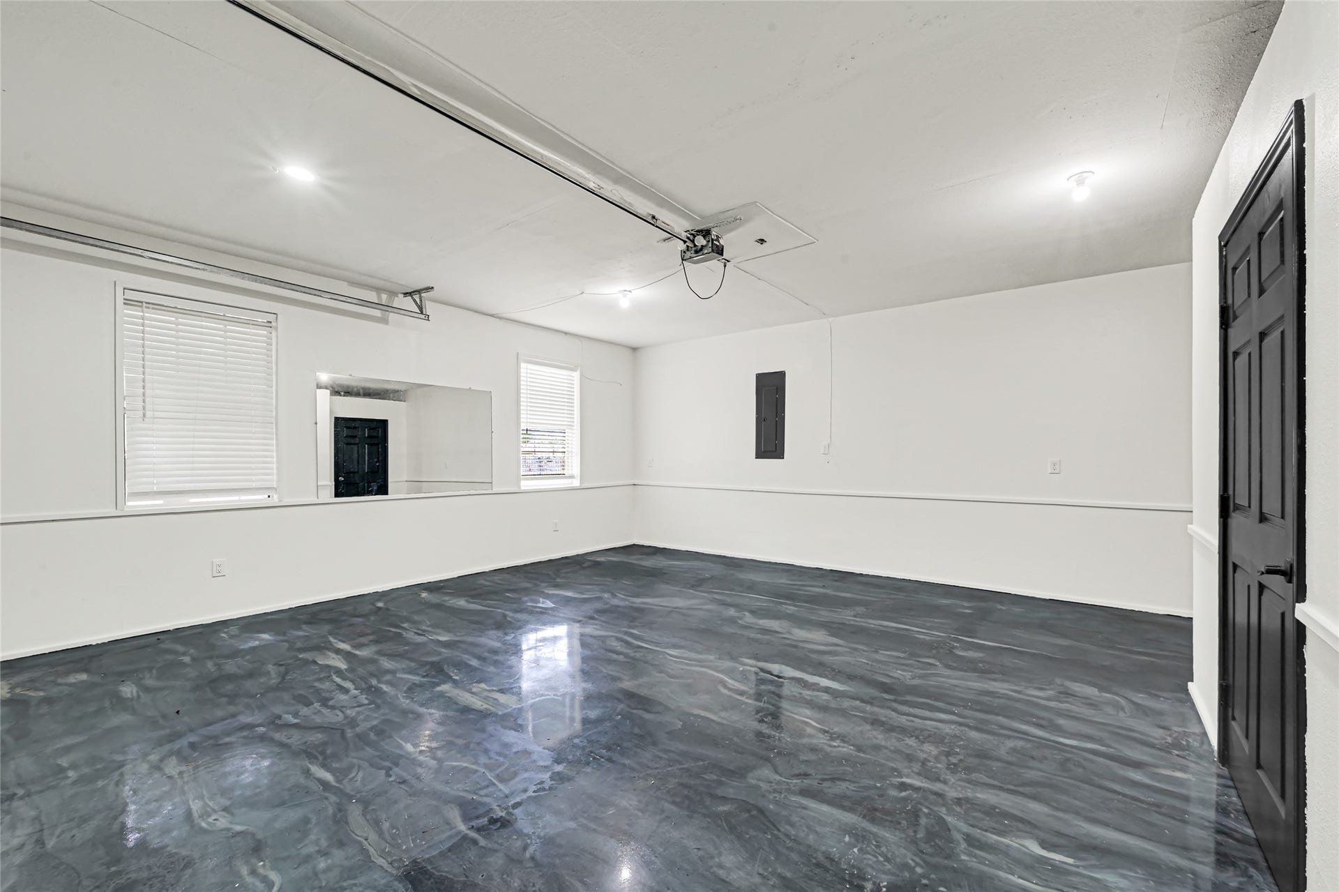 19763 Irenell Dr, Porter, TX 77365 Spacious and bright garage with sleek epoxy flooring, featuring ample natural light from two windows and convenient overhead storage.