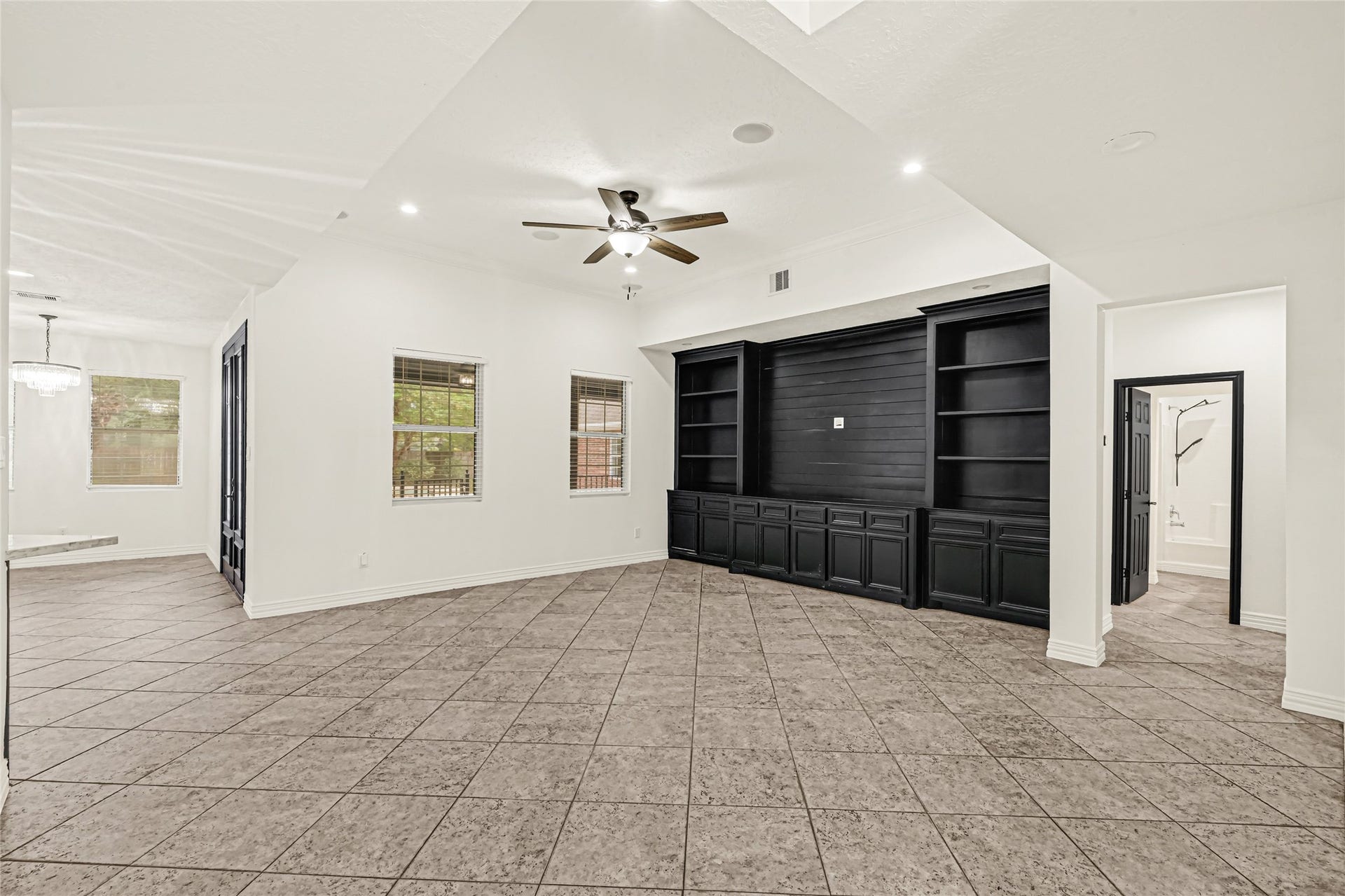 19763 Irenell Dr, Porter, TX 77365 Spacious living area features elegant tile flooring, a modern ceiling fan, and a striking black built-in entertainment center with ample shelving and storage.