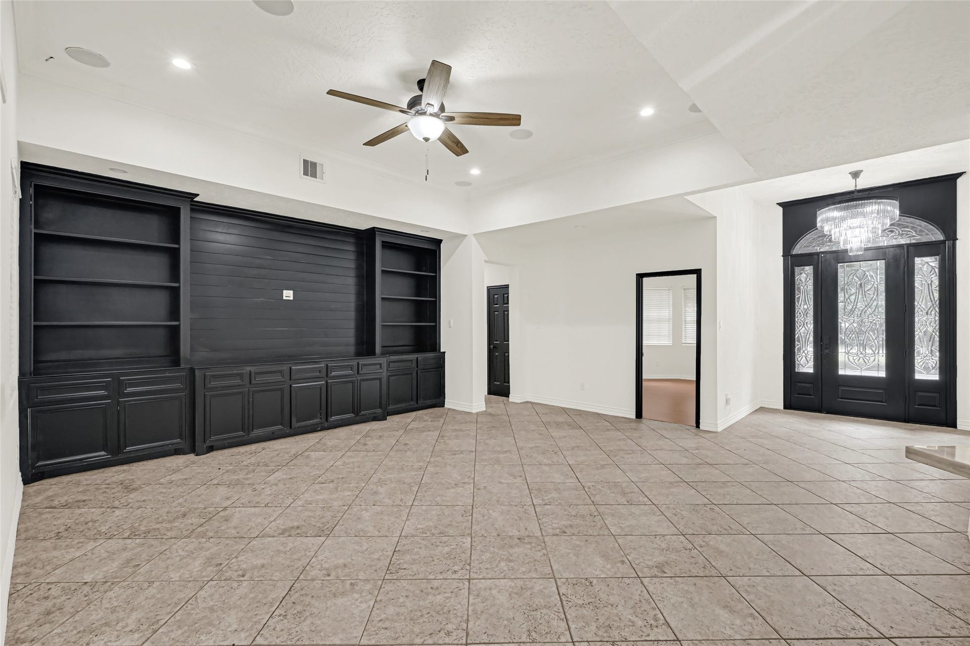 19763 Irenell Dr, Porter, TX 77365 Spacious living area featuring elegant built-in shelving, stylish tiled flooring, and a statement chandelier at the entrance, creating a welcoming atmosphere.