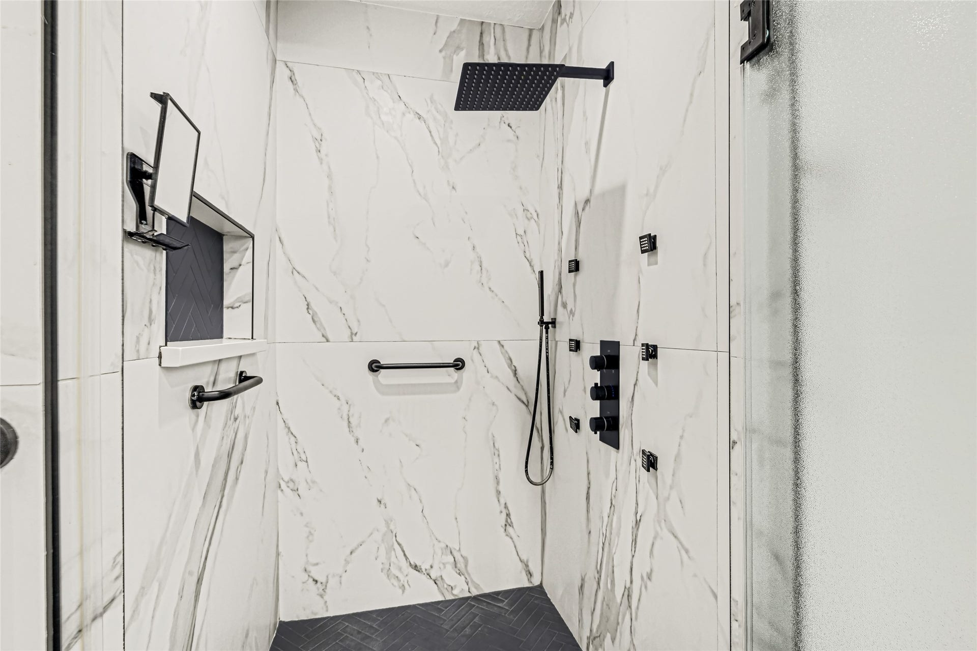 19763 Irenell Dr, Porter, TX 77365 Luxurious shower with sleek, marble-style walls, rainfall showerhead, and modern matte black fixtures for a spa-like experience.