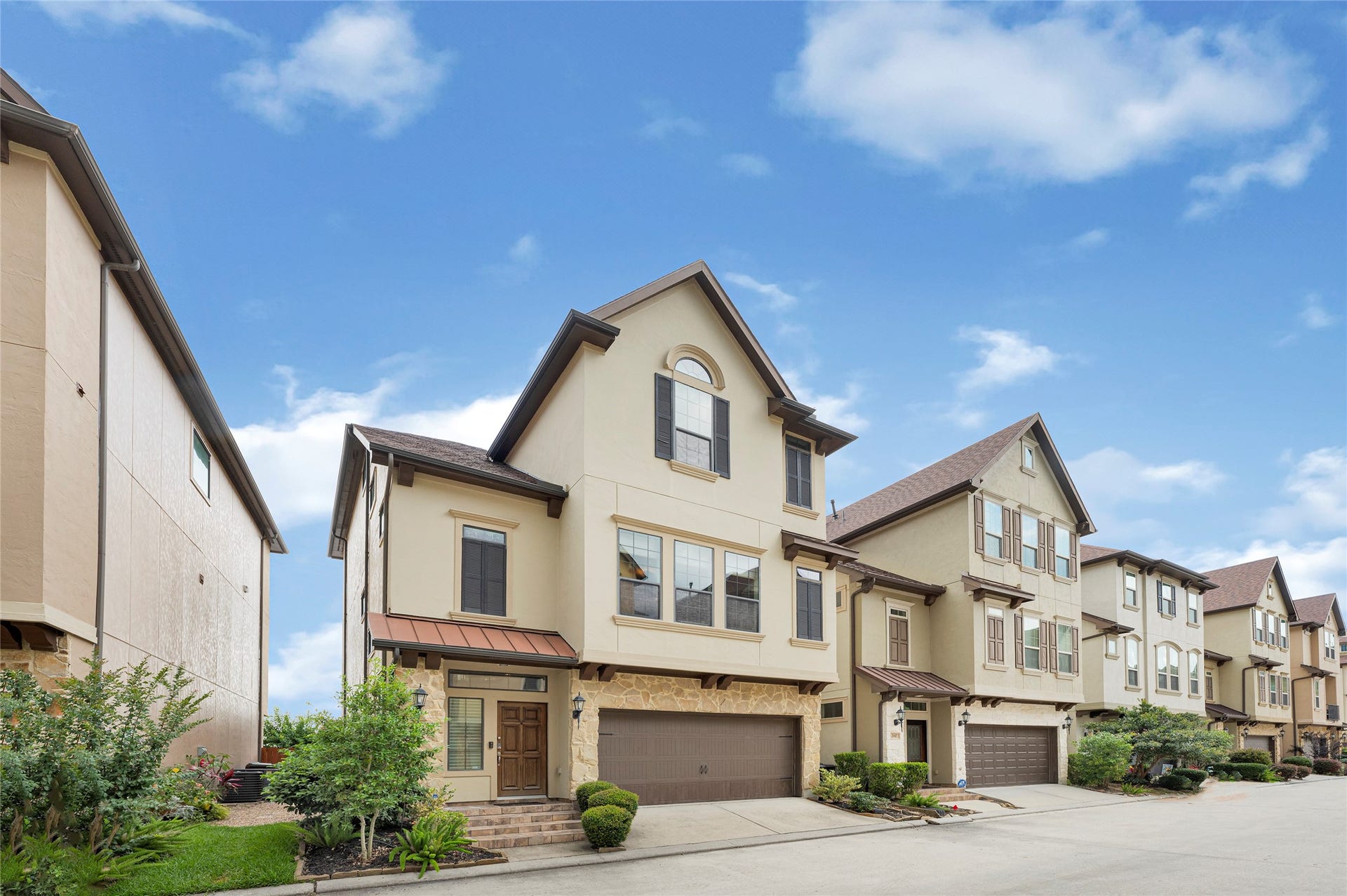 2815 Kings Retreat Circle, Kingwood, TX 77345 This property features a modern, multi-story townhouse with a stone and stucco exterior, a two-car garage, and a well-maintained front yard. It's part of a row of similar homes on a clean, quiet street under a clear blue sky.