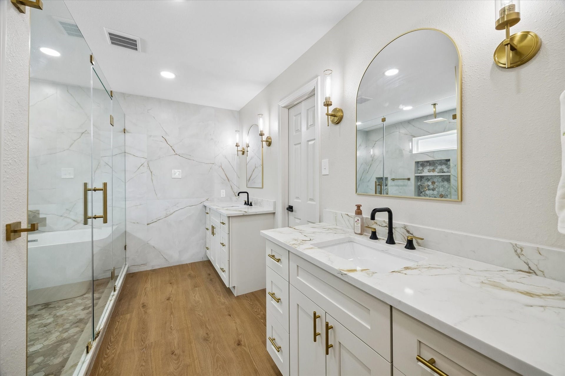 2302 Ashford Hollow Lane, Houston, TX 77077 Elegant bathroom featuring a spacious glass-enclosed shower, luxurious quartz countertops, and stylish gold fixtures, all complemented by warm wood looking flooring.
