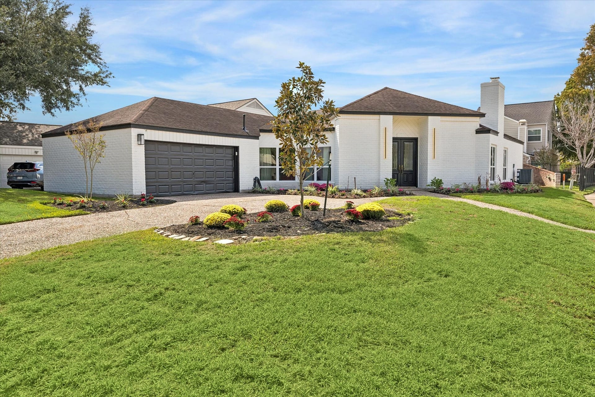 2302 Ashford Hollow Lane, Houston, TX 77077 Charming single-story home with a modern touch, featuring a spacious two-car garage, elegant white brick exterior, and a well-maintained front yard with lush landscaping.
