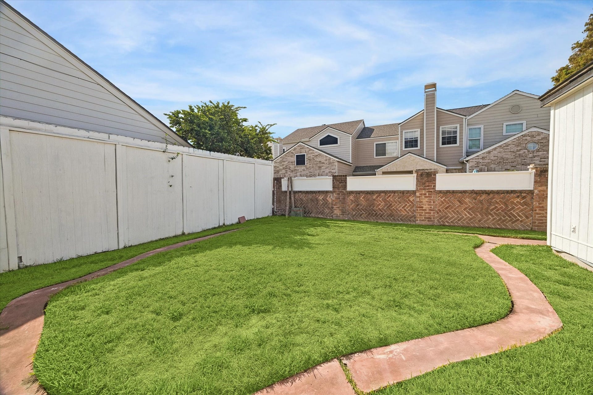 2302 Ashford Hollow Lane, Houston, TX 77077 Charming backyard with lush green lawn, bordered by a privacy fence and a unique brick wall, featuring a curved pathway for easy accessibility.