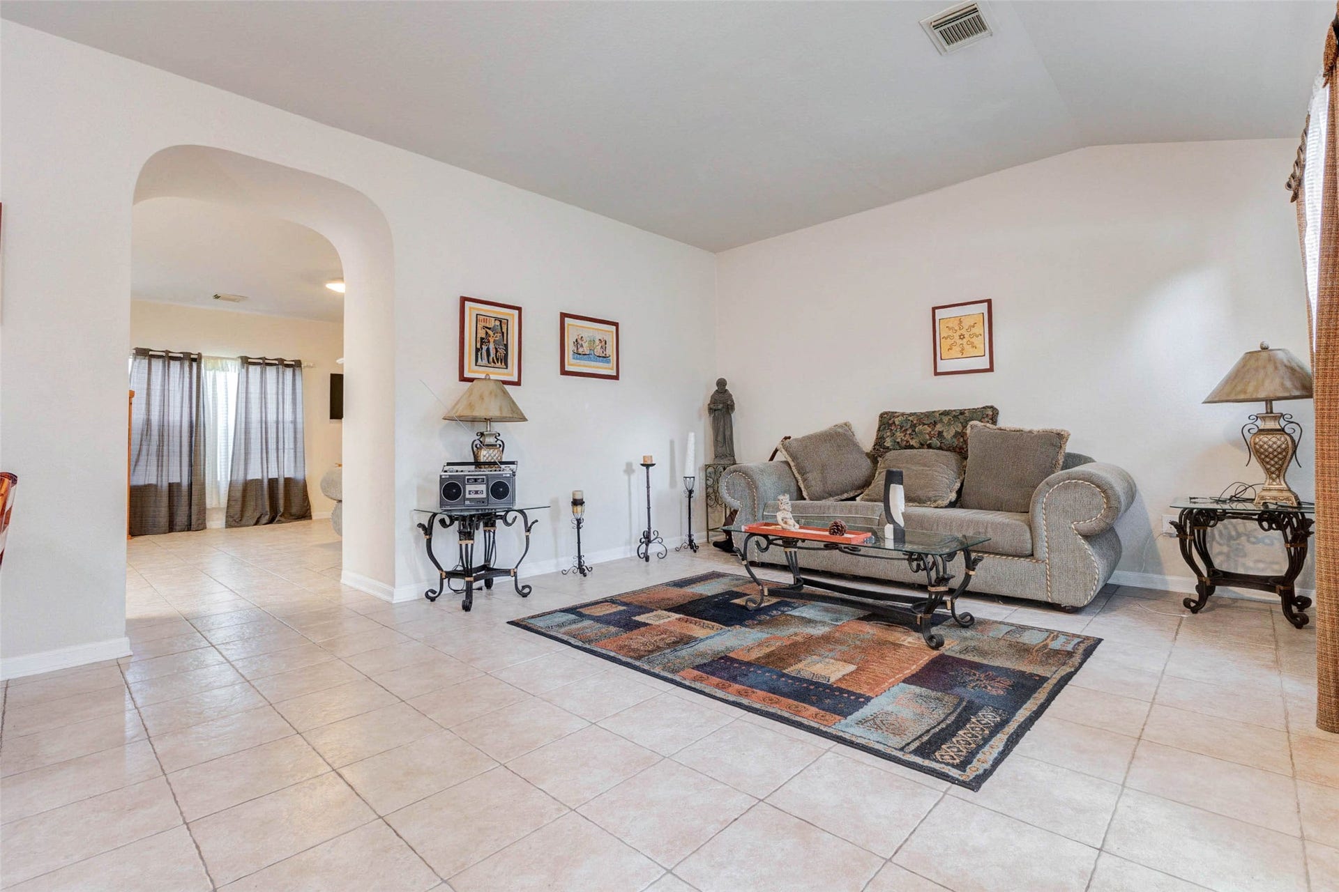 21211 Arcadia Park Lane, Humble, TX 77338 Comfortable living area featuring a cozy seating arrangement centered around a decorative rug and accent table. Natural light filters in from nearby windows, enhancing the warm and inviting atmosphere. The open layout connects effortlessly to other parts of the home, while neutral walls and tile flooring create a versatile space ready for your personal style and everyday relaxation.