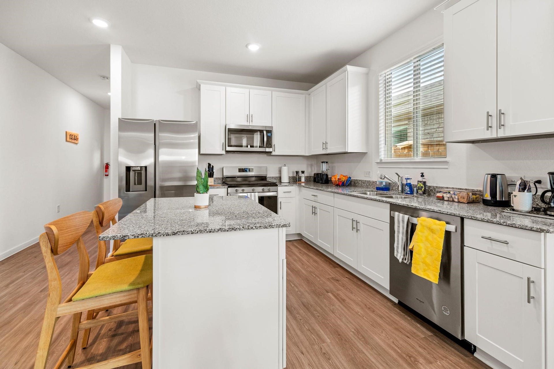 1301 Bright Hill Drive, Katy, TX 77493 Modern kitchen with sleek stainless steel appliances, granite countertops, and ample white cabinetry, complemented by a cozy breakfast bar and warm wood flooring.
